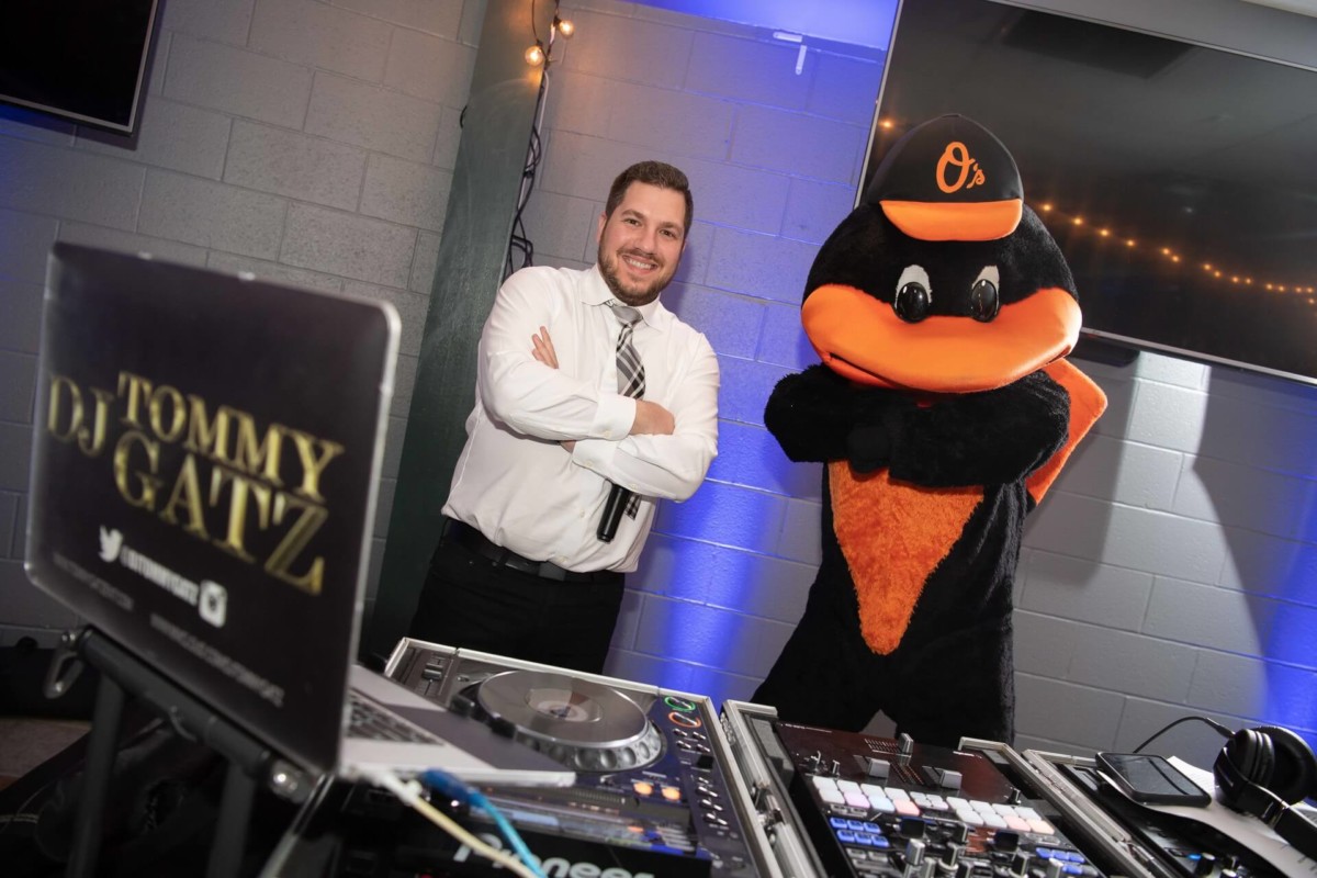 Heather-Scott-Wedding-Low-Res-139 1 - TOMMY GATZ ENTERTAINMENT DJ next to person in a bird mascot costume behind a DJ booth with equipment and sign reading "Tommy DJ Gatz" in a decorated room.