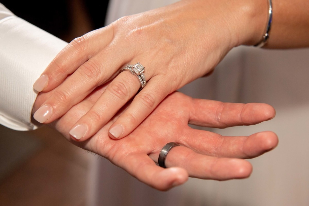 Heather-Scott-Wedding-Low-Res-151 1 - TOMMY GATZ ENTERTAINMENT Close-up of two hands with rings, showing a wedding band on one hand and an engagement ring on the other.