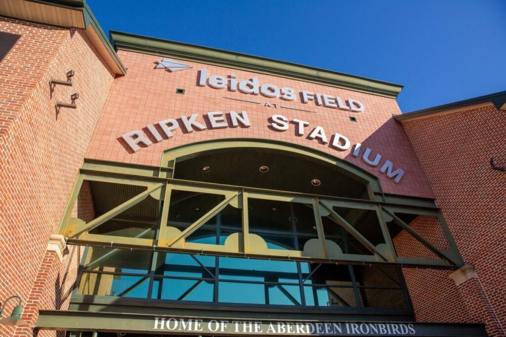 Heather-Scott-Wedding-Low-Res-38 1 - TOMMY GATZ ENTERTAINMENT Entrance of Leidos Field at Ripken Stadium with the Aberdeeen IronBirds sign visible above. Red brick exterior and clear blue sky.