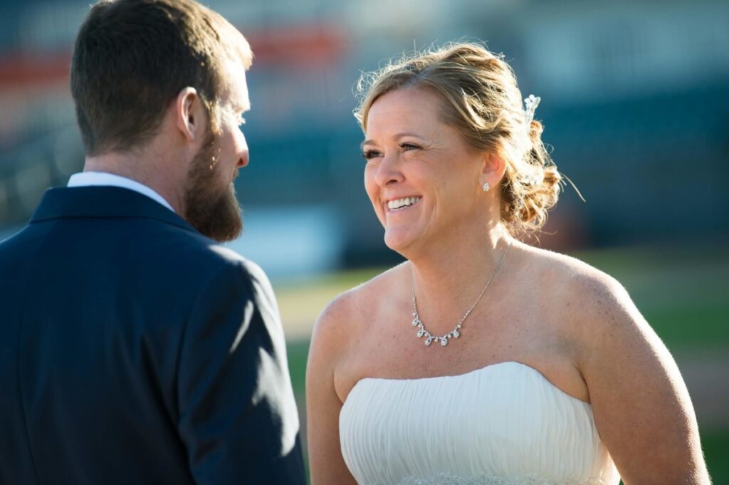 Heather-Scott-Wedding-Low-Res-45 1 - TOMMY GATZ ENTERTAINMENT A bride and groom are outdoors, smiling at each other. The bride wears a strapless white dress, and the groom is in a dark suit. The scene is sunlit.