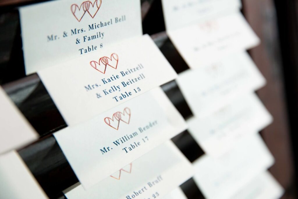 Heather-Scott-Wedding-Low-Res-57 1 - TOMMY GATZ ENTERTAINMENT Close-up of wedding place cards featuring names and table assignments, with heart motifs at the top of each card.