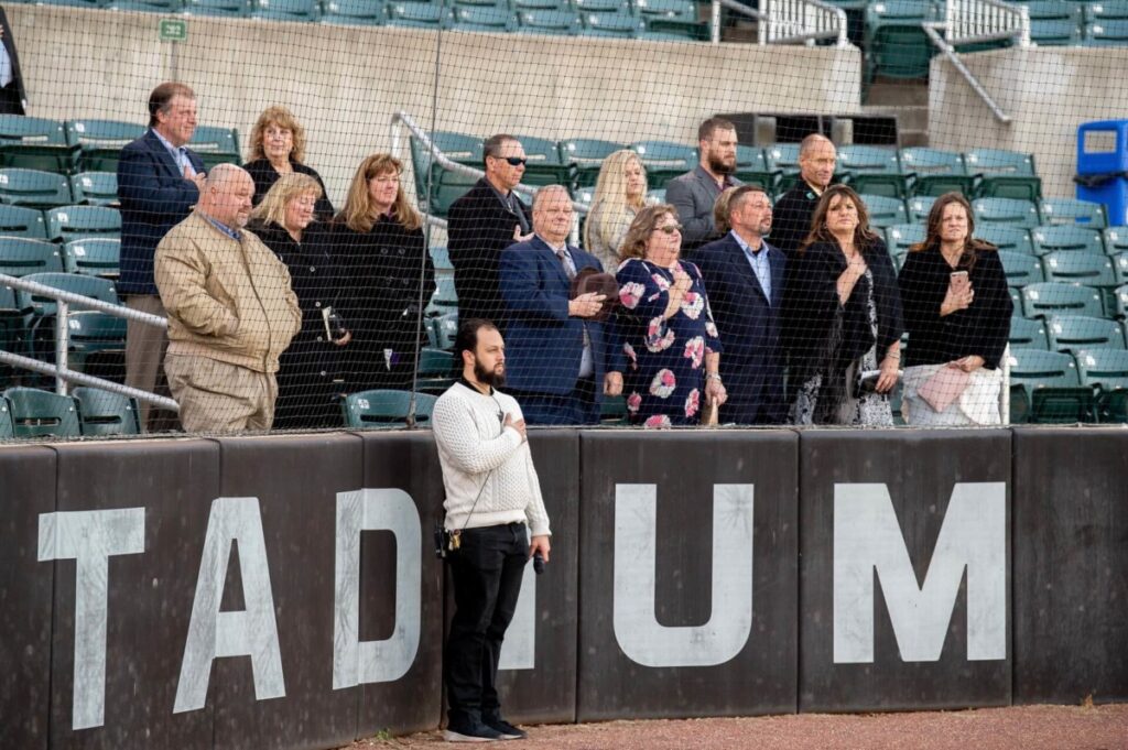 Heather-Scott-Wedding-Low-Res-68 1 - TOMMY GATZ ENTERTAINMENT People standing in a stadium with hands over their hearts, observing a ceremony or anthem.