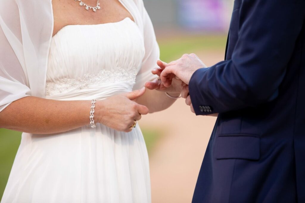 Heather-Scott-Wedding-Low-Res-89 1 - TOMMY GATZ ENTERTAINMENT Close-up of a bride and groom exchanging rings during a wedding ceremony, with the bride in a white dress and the groom in a dark suit.