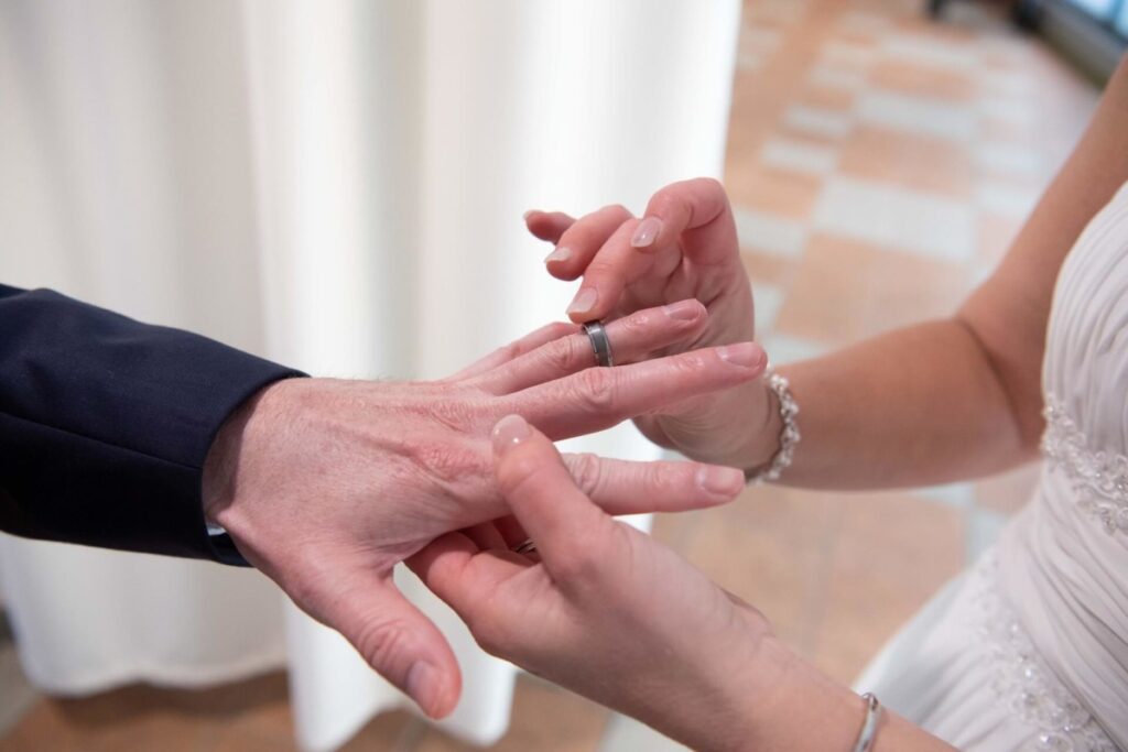 Heather-Scott-Wedding-Low-Res-95 1 - TOMMY GATZ ENTERTAINMENT A bride places a ring on the groom's finger during a wedding ceremony.