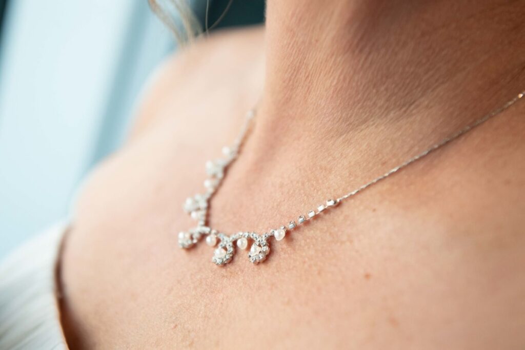 Heather-Scott-Wedding-Low-Res-97 1 - TOMMY GATZ ENTERTAINMENT Close-up of a silver necklace with dangling pearls worn by a person.