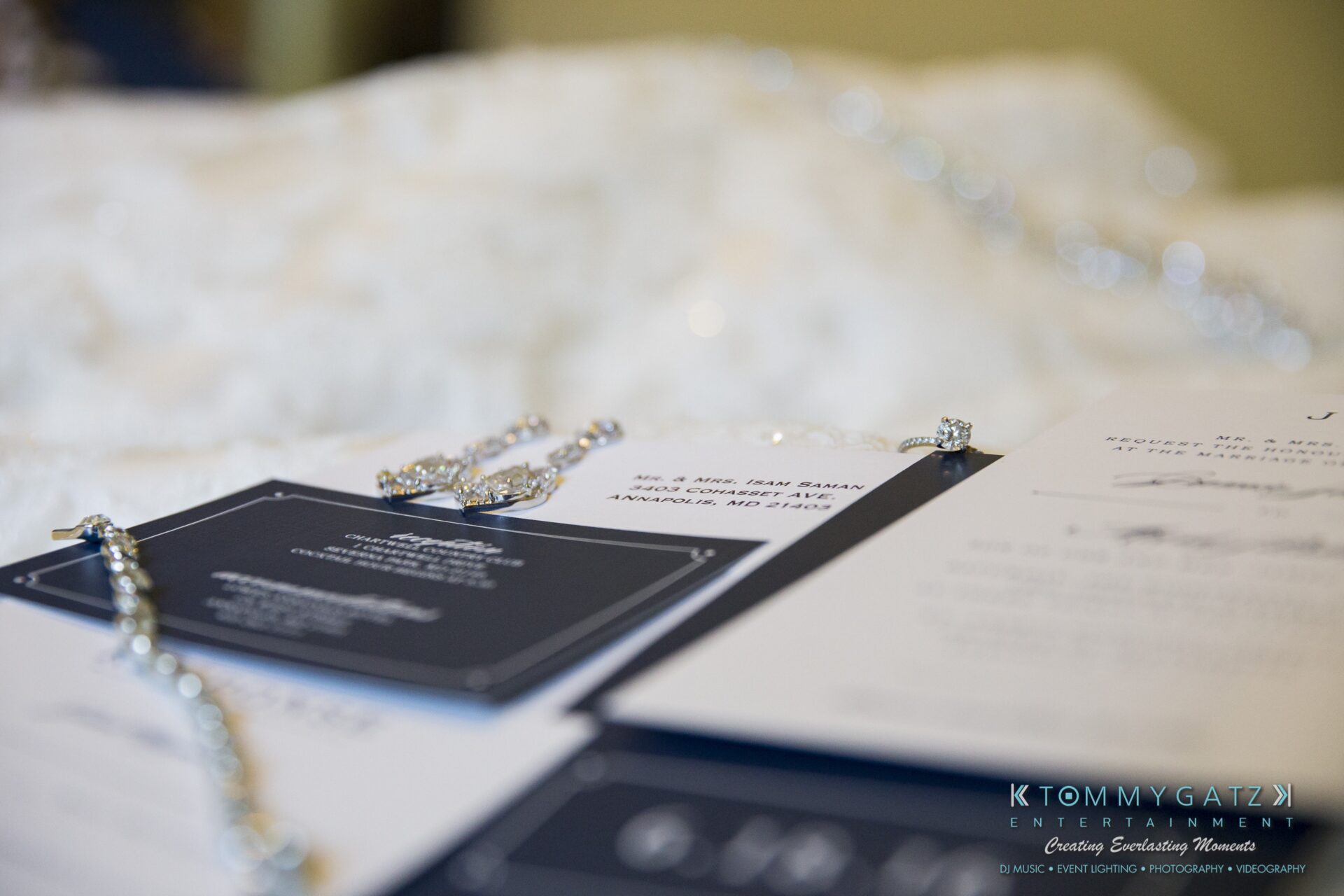 Jamie-and-Mark-Low-Res-Watermark-11 - TOMMY GATZ ENTERTAINMENT Close-up of a wedding invitation with elegant script on textured paper, accompanied by a thin, sparkly bracelet.
