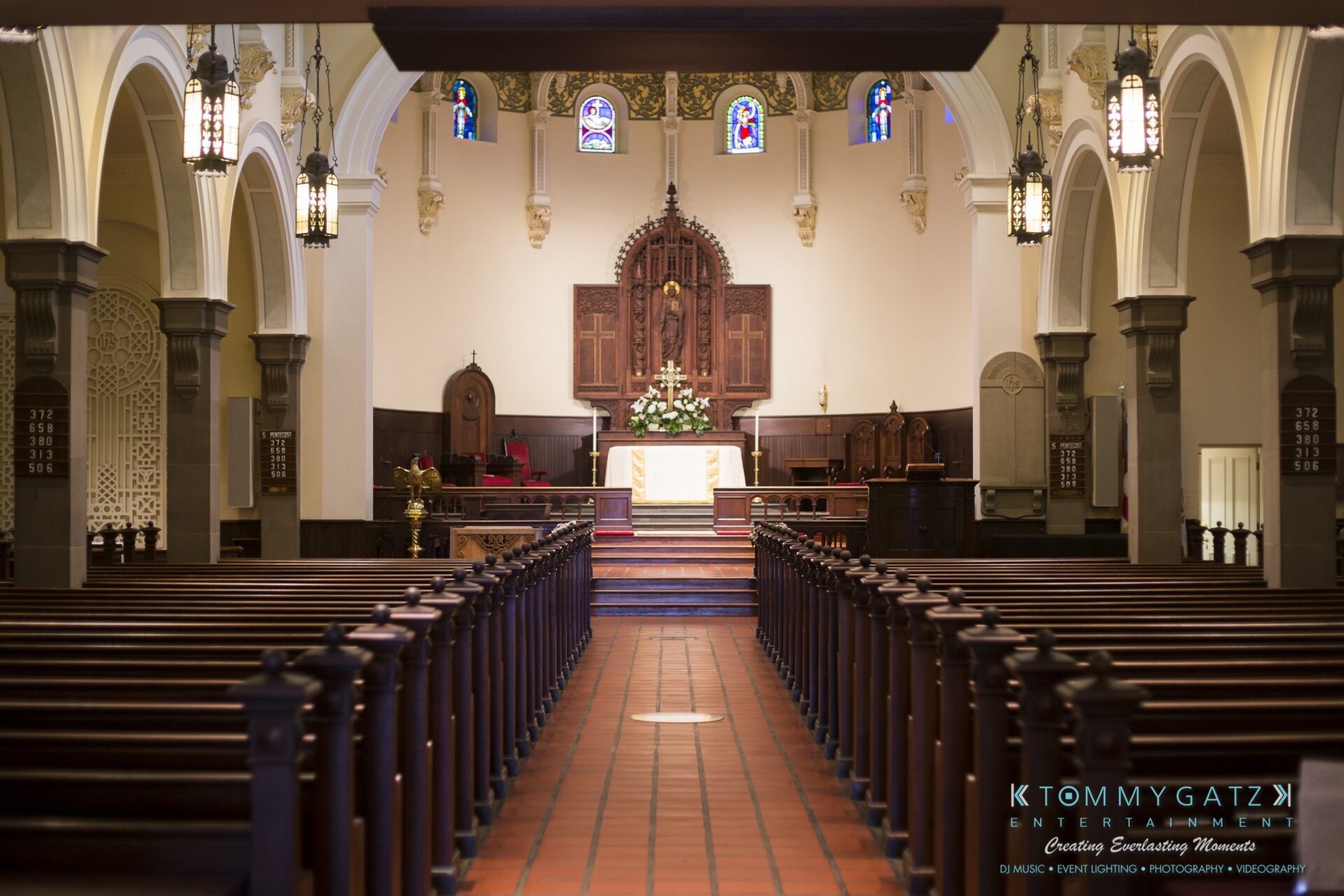 Jamie-and-Mark-Low-Res-Watermark-14 - TOMMY GATZ ENTERTAINMENT Interior of a church with empty wooden pews, ornate altar, and stained glass windows, creating a serene, sacred atmosphere.