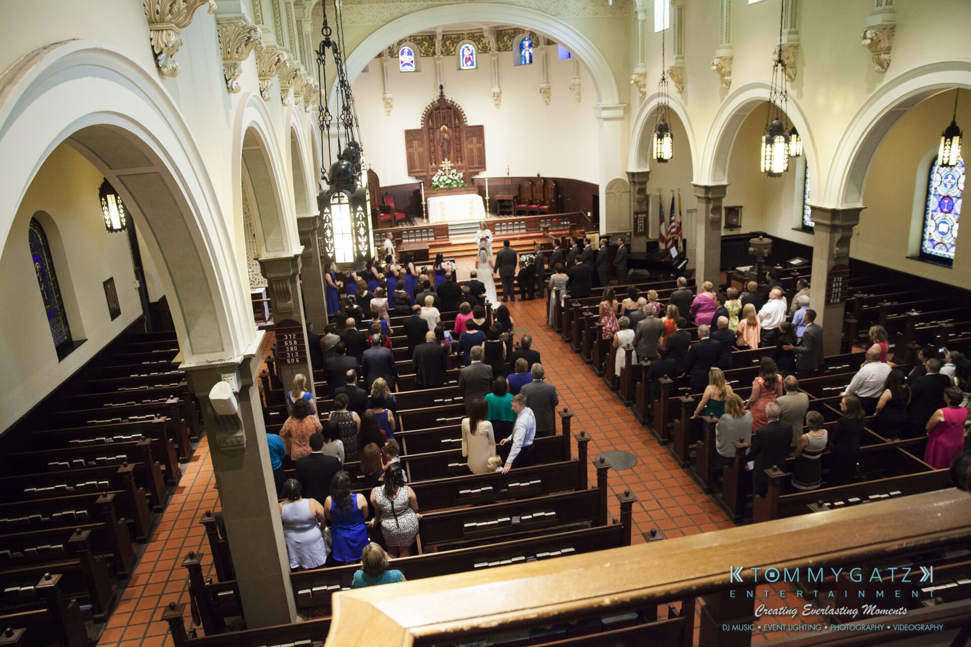 Jamie-and-Mark-Low-Res-Watermark-206 - TOMMY GATZ ENTERTAINMENT Aerial view of a church interior during a wedding ceremony, with guests seated in pews and the couple standing at the altar.