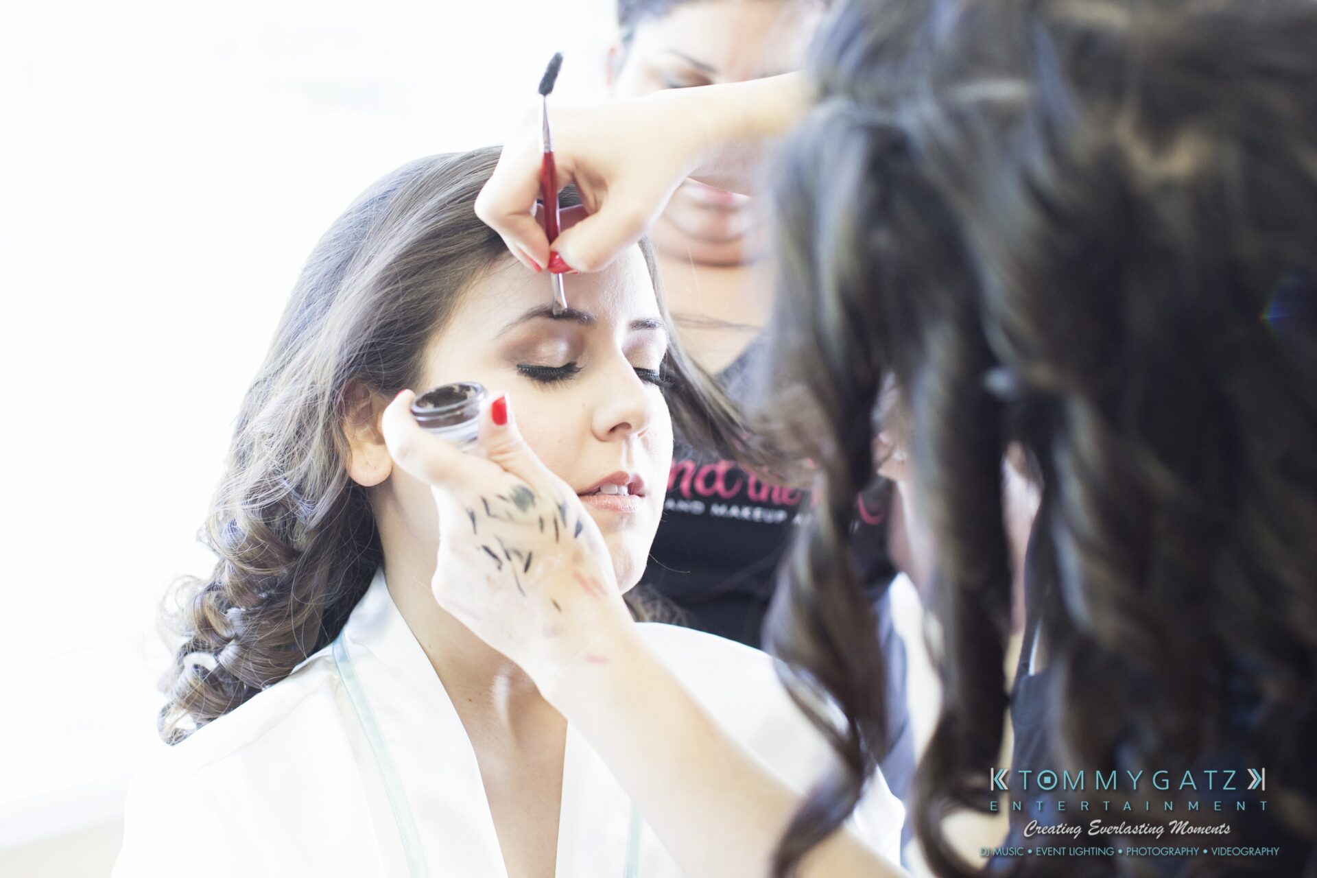 Jamie-and-Mark-Low-Res-Watermark-7-1 - TOMMY GATZ ENTERTAINMENT Person getting makeup applied by a makeup artist.