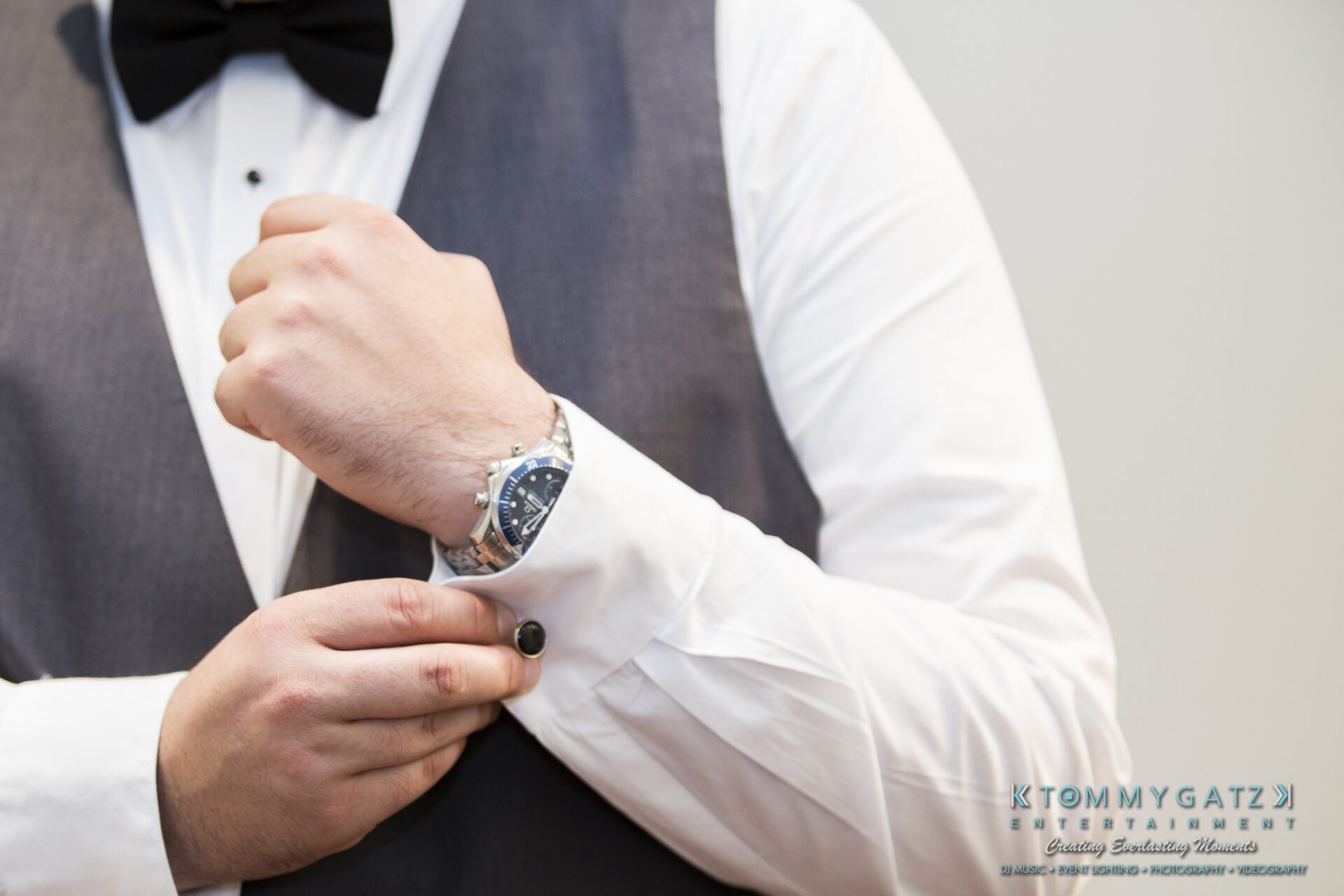 Jamie-and-Mark-Low-Res-Watermark-76 - TOMMY GATZ ENTERTAINMENT A man in formal attire adjusts his cufflink. He wears a dark waistcoat, white shirt, black bow tie, and watch on his left wrist.