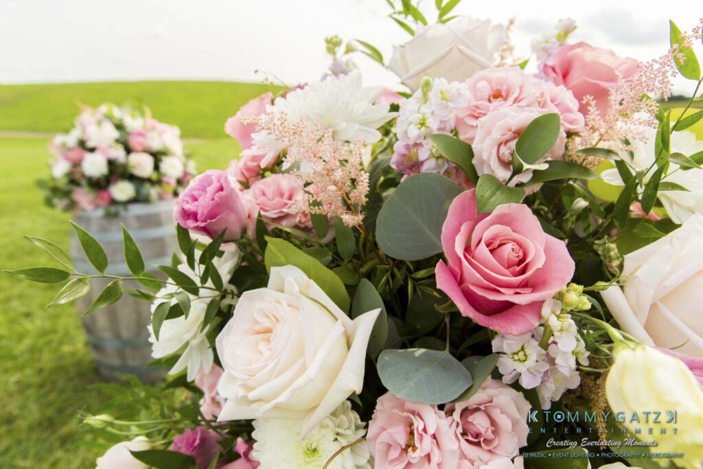 Jennifer-Rudi-Highlights-Low-res-3 - TOMMY GATZ ENTERTAINMENT Bouquet of pink and white flowers with greenery, displayed outdoors with a grassy field in the background.