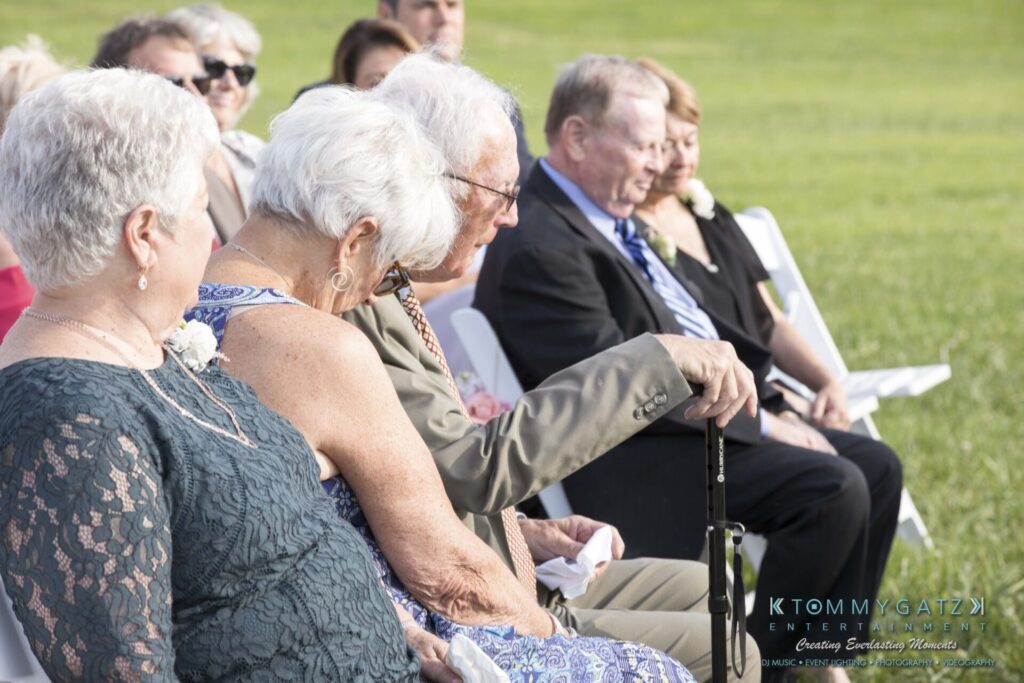 JenniferRudiWeddingCeremonyPhotos-104 - TOMMY GATZ ENTERTAINMENT A group of older adults seated outdoors in formal attire, attending an event.
