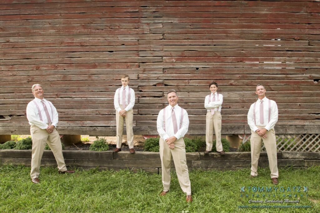 JenniferRudiWeddingFormalPhotos-206 - TOMMY GATZ ENTERTAINMENT Five people in coordinated outfits stand in front of a rustic, wooden barn wall.