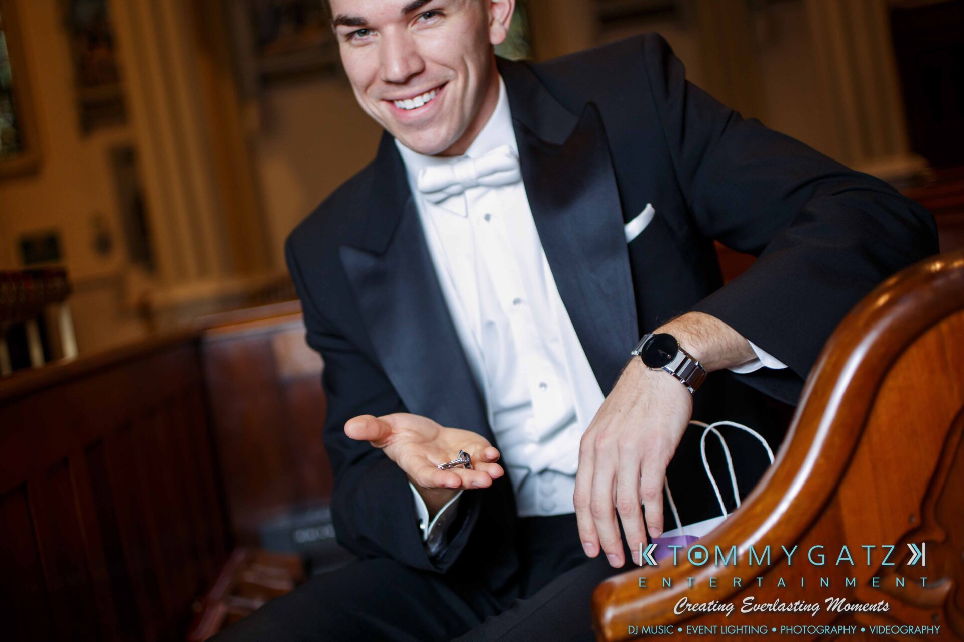 JulieKyleLongWedding11715-39 - TOMMY GATZ ENTERTAINMENT Person in formal attire sitting on a bench, smiling, holding a small object in their hand.