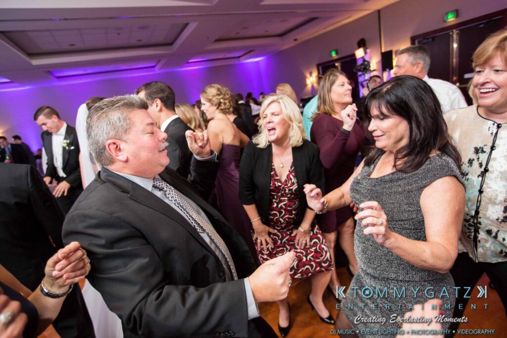 JulieKyleLongWedding11715-659 - TOMMY GATZ ENTERTAINMENT People dancing at a formal event in a decorated ballroom with purple lighting.