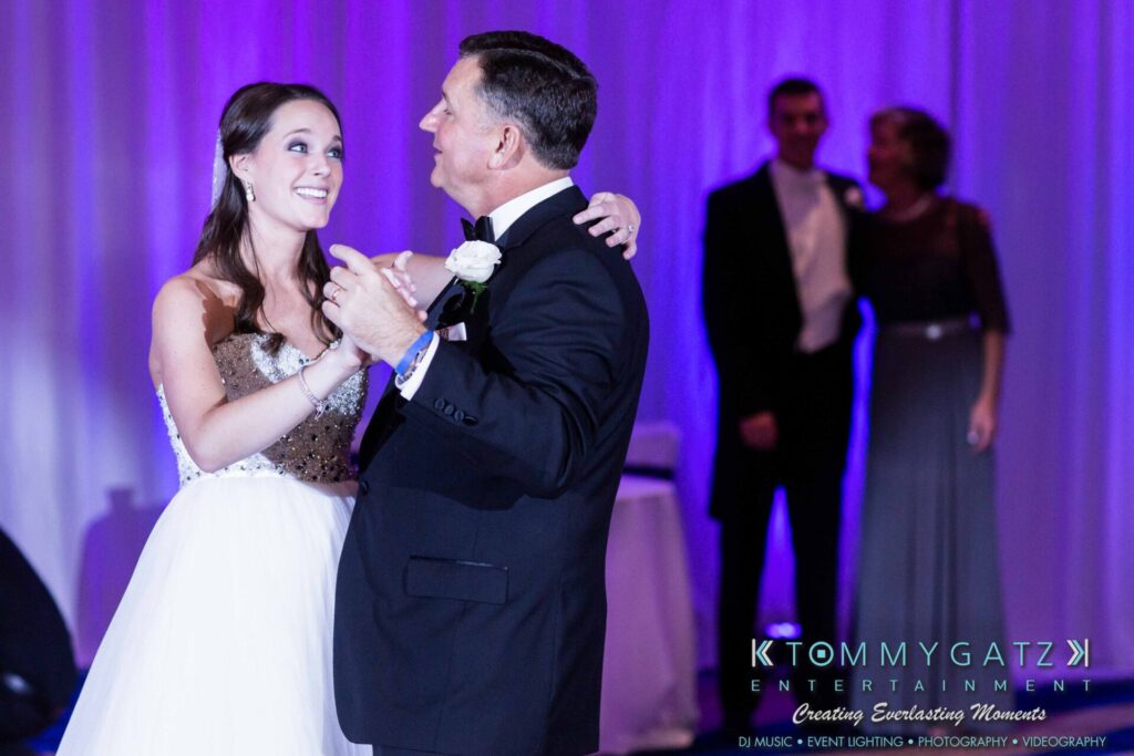 JulieKyleLongWedding11715-792 - TOMMY GATZ ENTERTAINMENT A bride and an older man share a dance at an event, with people observing in the background.