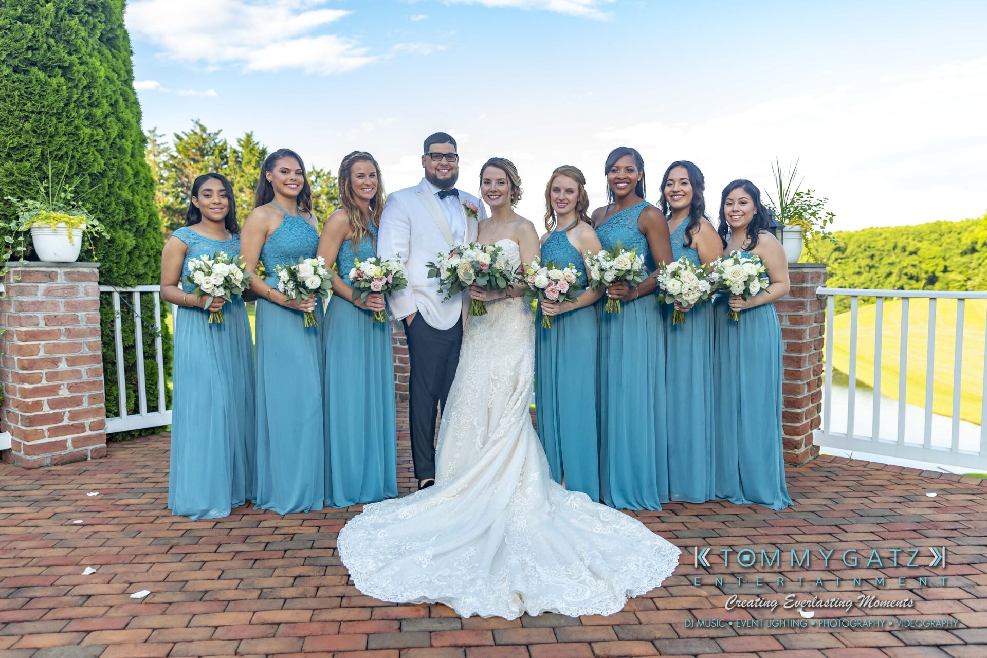 Kari-Jose-062318-FORMALS-Low-Res-WM-359 - TOMMY GATZ ENTERTAINMENT A bridal party poses for a photo outdoors. The group includes the bride, groom, and seven bridesmaids in teal dresses, holding bouquets.