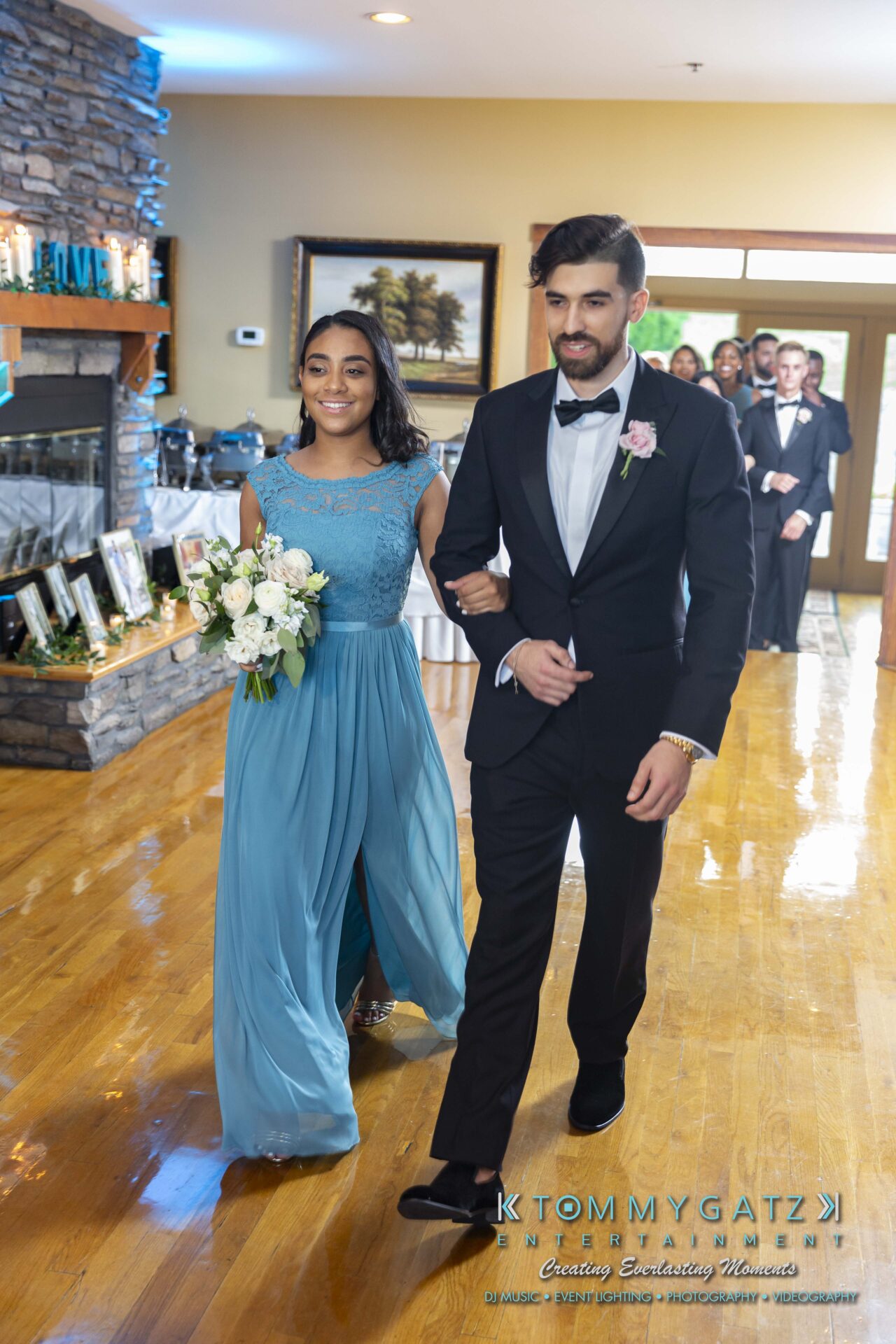 Kari-Jose-062318-RECEPTION-Low-Res-WM-440 - TOMMY GATZ ENTERTAINMENT A couple in formal attire walks down a hallway; the woman holds a bouquet, and the man wears a suit with a boutonniere.