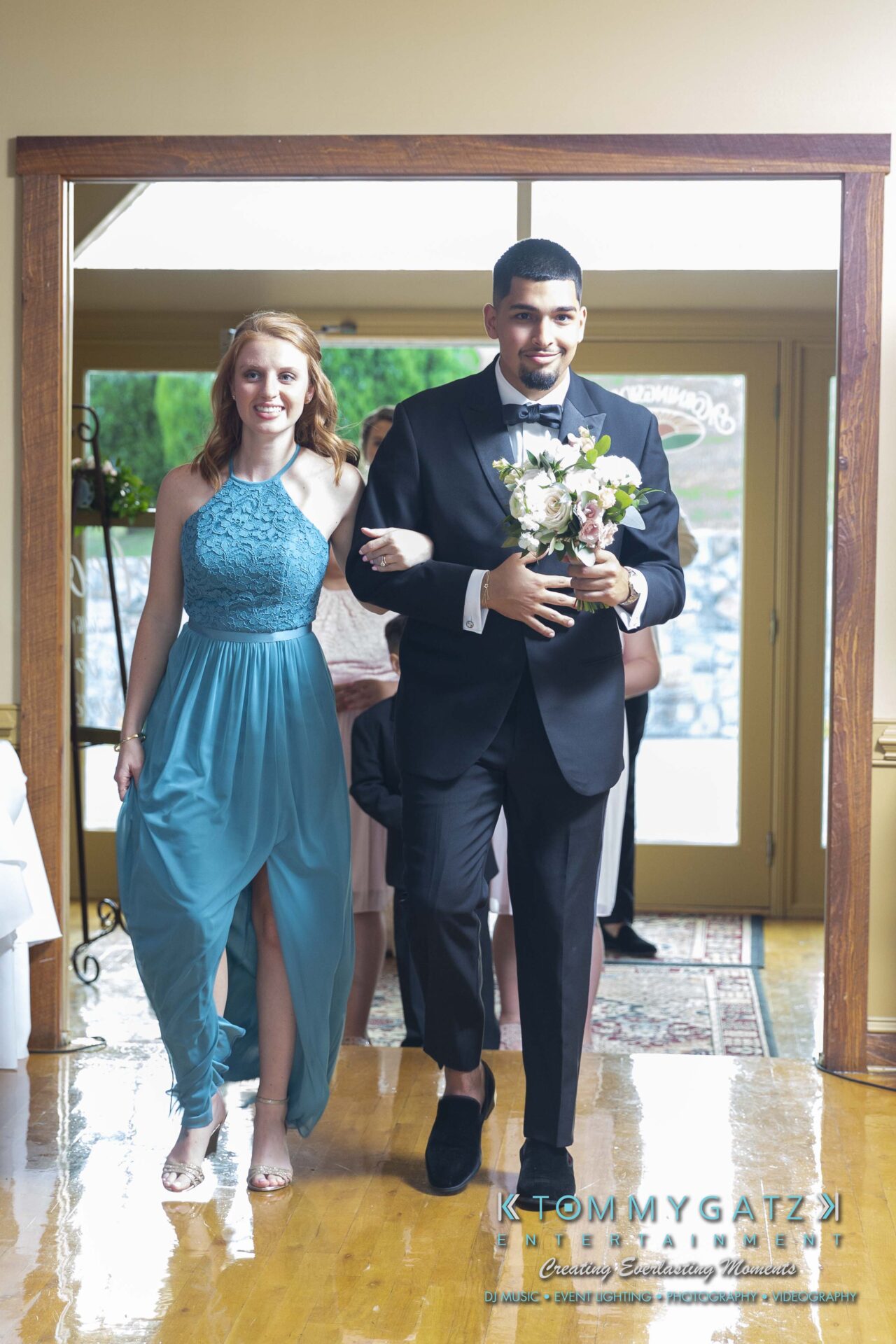 Kari-Jose-062318-RECEPTION-Low-Res-WM-448 - TOMMY GATZ ENTERTAINMENT A man in a suit and a woman in a blue dress walk arm-in-arm through a doorway. The man holds a bouquet.