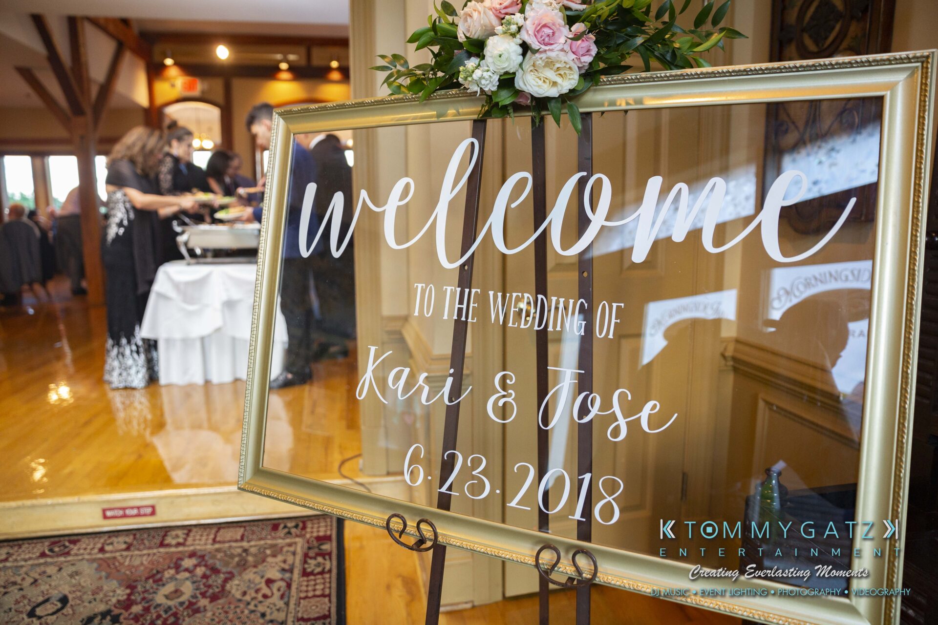 Kari-Jose-062318-RECEPTION-Low-Res-WM-512 - TOMMY GATZ ENTERTAINMENT A welcome sign reads "Welcome to the Wedding of Kari & Jose, 6-23-2018" in front of a reception area with guests and a buffet table.