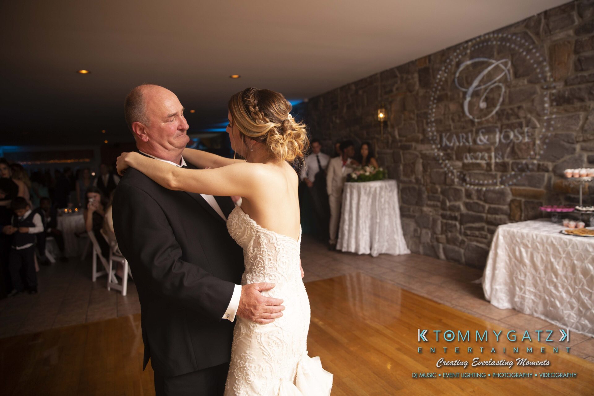 Kari-Jose-062318-RECEPTION-Low-Res-WM-532 - TOMMY GATZ ENTERTAINMENT A bride and an older man, possibly her father, sharing a dance in a wedding reception hall. A wedding cake is visible in the background.