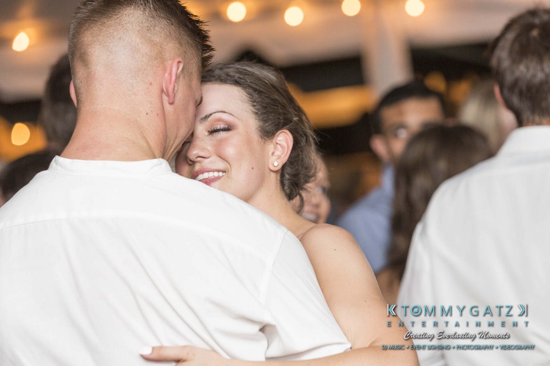 Keara-Patrick-Wedding-51218-FINALS-Low-Res-WM-20 - TOMMY GATZ ENTERTAINMENT A couple dancing closely at an event, surrounded by other attendees in a warmly lit setting.