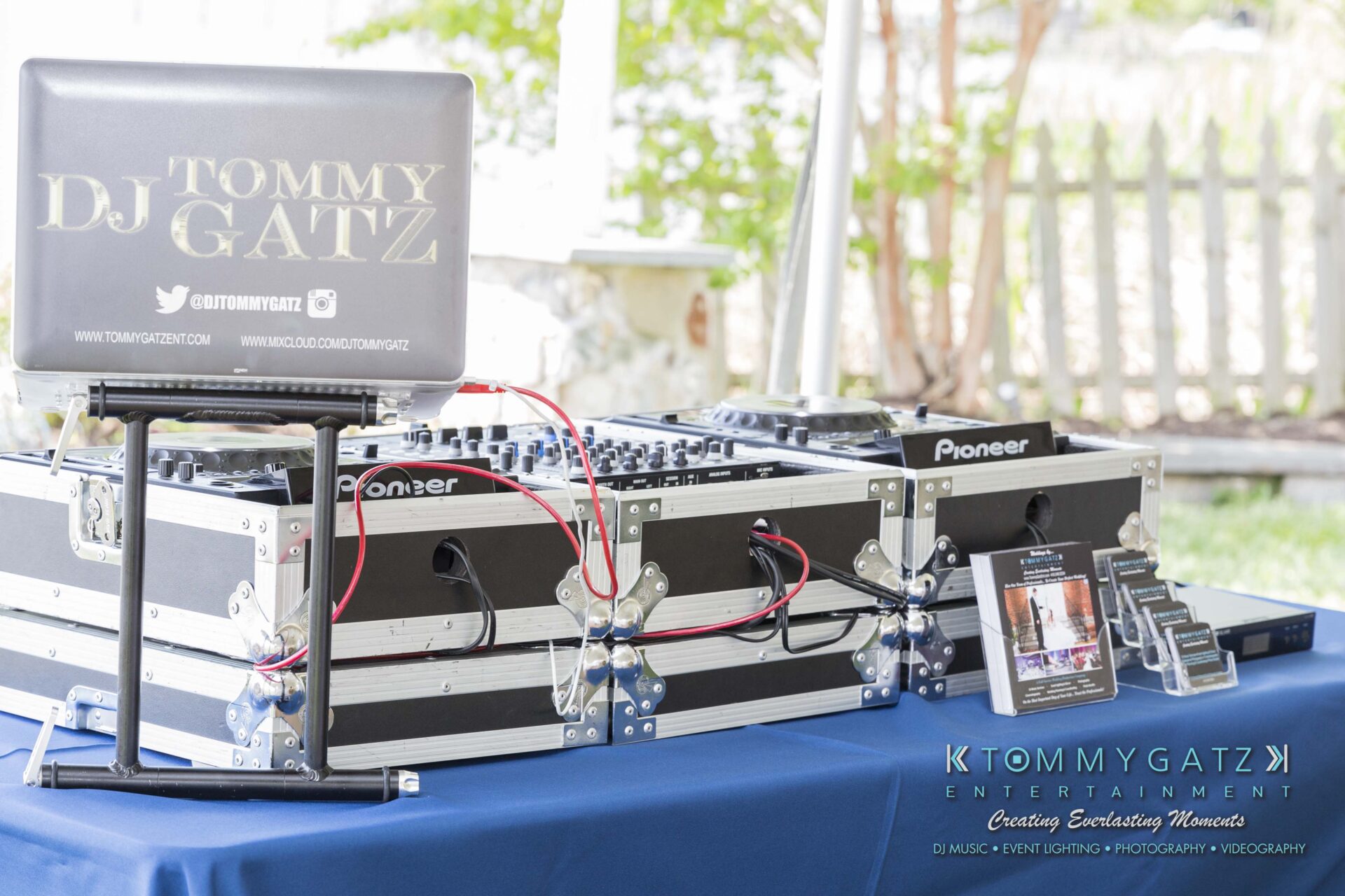 Keara-Patrick-Wedding-51218-FINALS-Low-Res-WM-5 - TOMMY GATZ ENTERTAINMENT DJ setup with mixing equipment and laptop on a blue table. Signs display "Tommy Gatz Entertainment" and social media information.