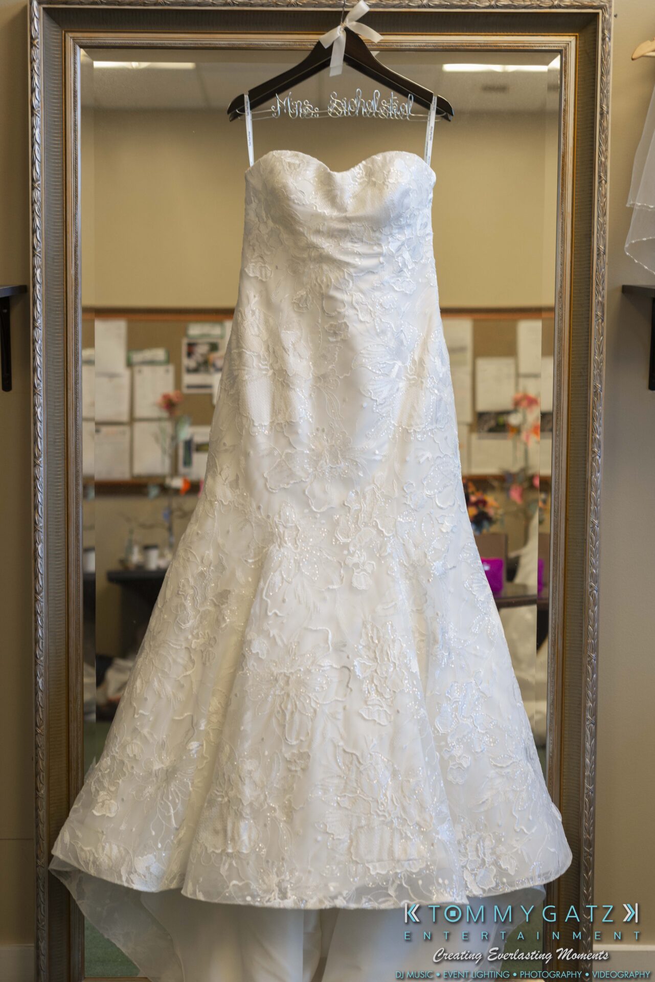 Lisa-Robert-092218-BLOG-selections-WM-1 - TOMMY GATZ ENTERTAINMENT A strapless white lace wedding dress hangs on a wooden hanger in front of a large mirror.