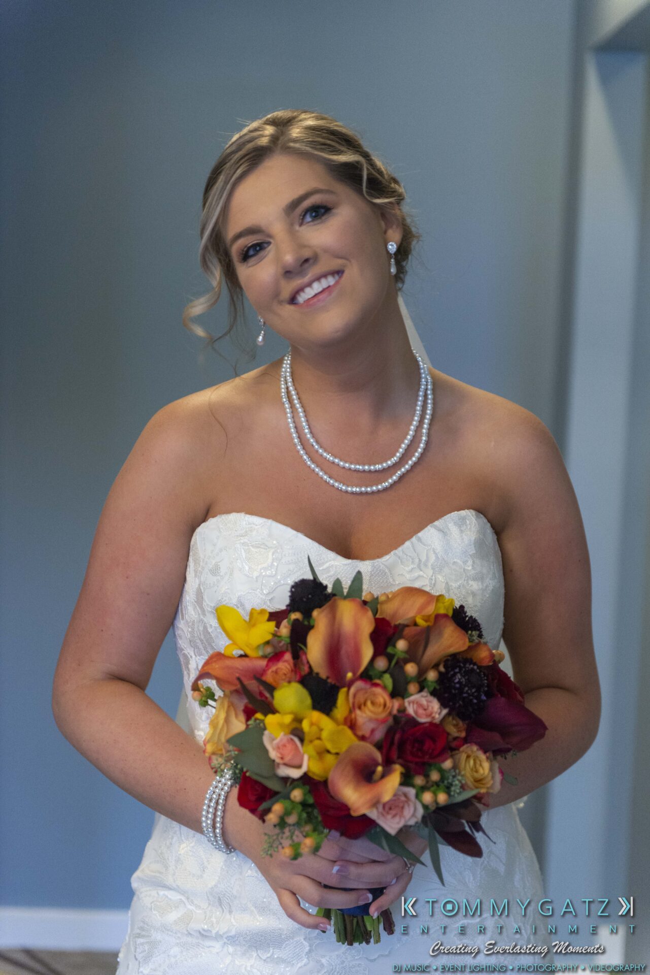 Lisa-Robert-092218-BLOG-selections-WM-12 - TOMMY GATZ ENTERTAINMENT A bride in a strapless white dress holds a colorful bouquet. She is smiling and wearing a pearl necklace and earrings.