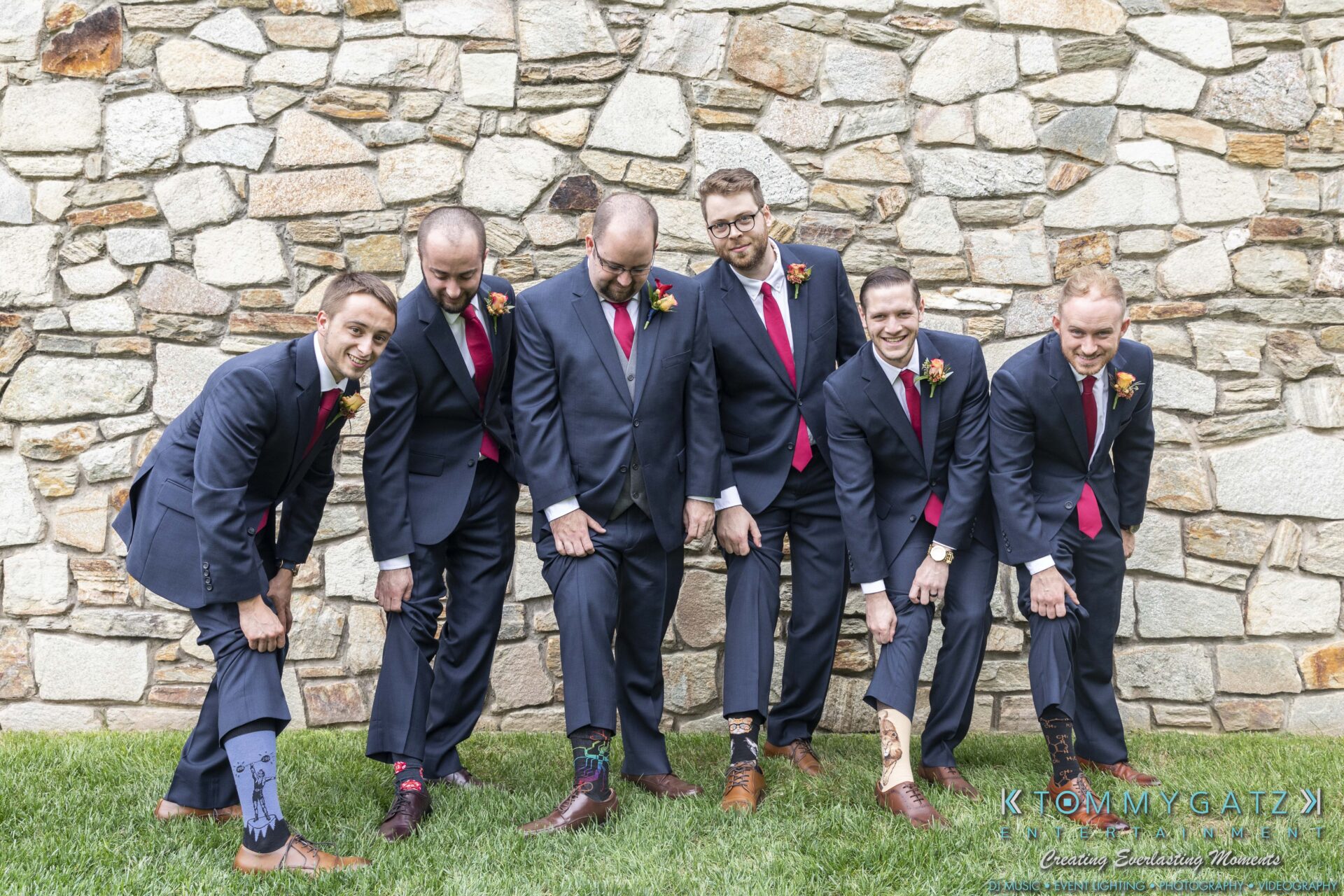 Lisa-Robert-092218-BLOG-selections-WM-14 - TOMMY GATZ ENTERTAINMENT Six men in suits stand outdoors, showing off colorful socks, against a stone wall backdrop.