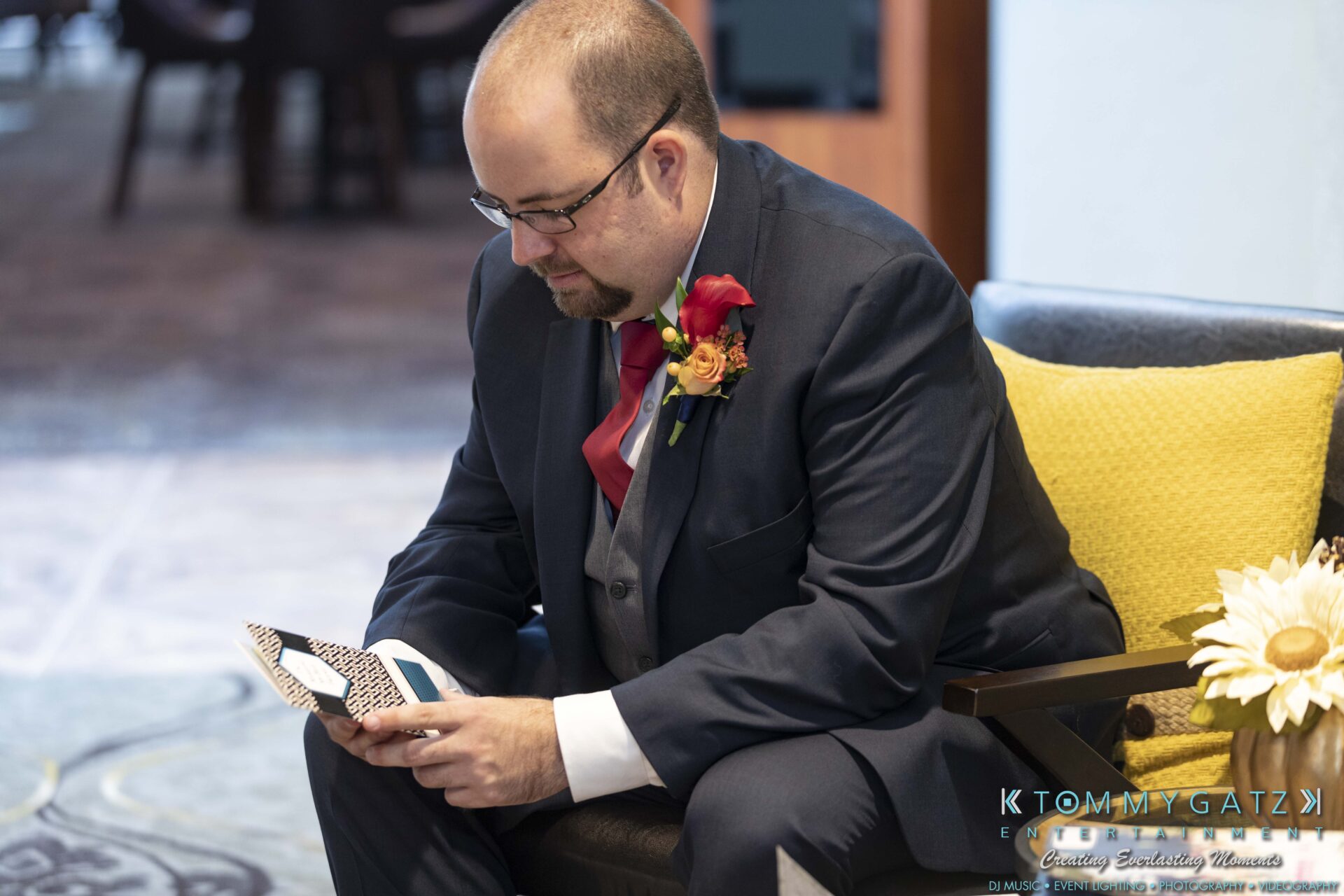 Lisa-Robert-092218-BLOG-selections-WM-24 - TOMMY GATZ ENTERTAINMENT A man in a suit sits on a chair, holding a folded piece of paper, with flowers on his lapel and next to him.