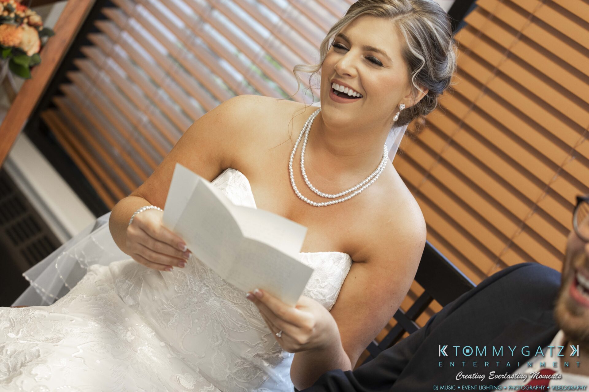 Lisa-Robert-092218-BLOG-selections-WM-28 - TOMMY GATZ ENTERTAINMENT Bride smiling while reading a note, sitting next to a person. They're indoors, with blinds in the background and "KTOMMY GATZ ENTERTAINMENT" text on the image.