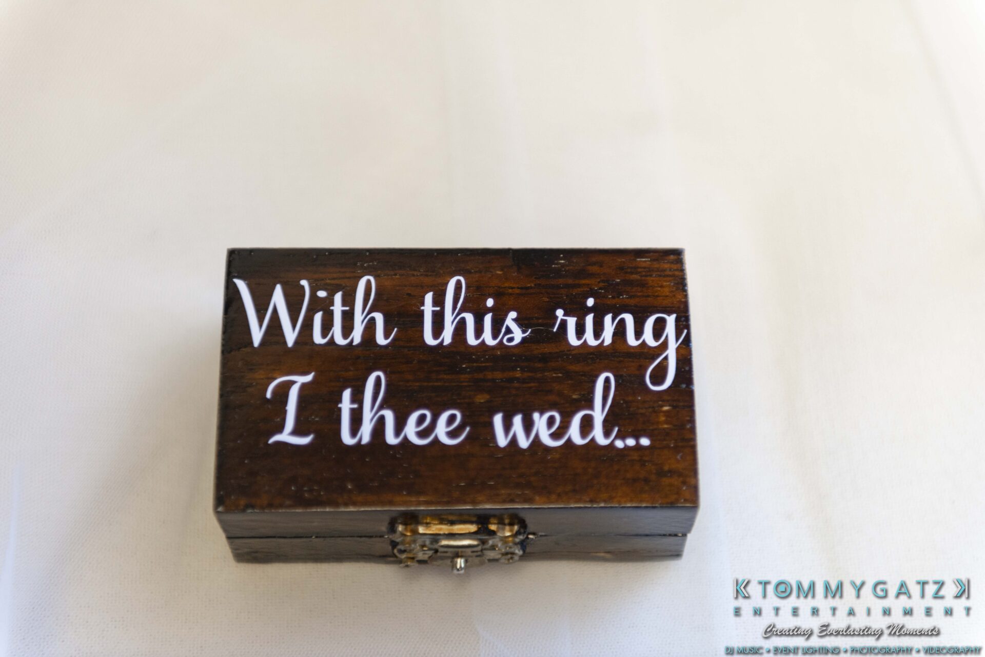 Lisa-Robert-092218-BLOG-selections-WM-3 - TOMMY GATZ ENTERTAINMENT A small wooden box with white text saying "With this ring, I thee wed" on the lid, placed on a white surface.