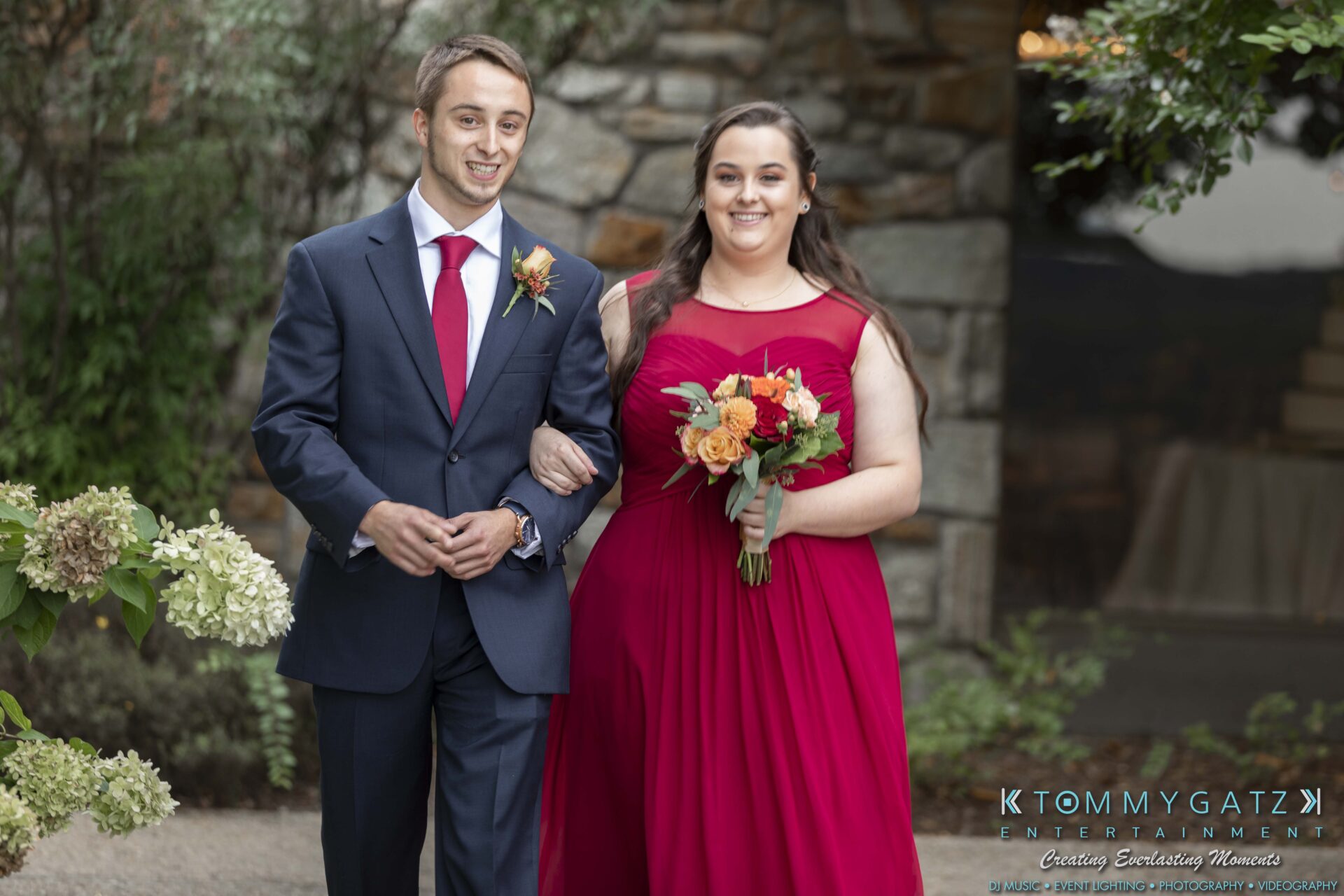 Lisa-Robert-092218-BLOG-selections-WM-45 - TOMMY GATZ ENTERTAINMENT A man and woman in formal attire, with the woman holding a bouquet, walk arm in arm down a garden path.