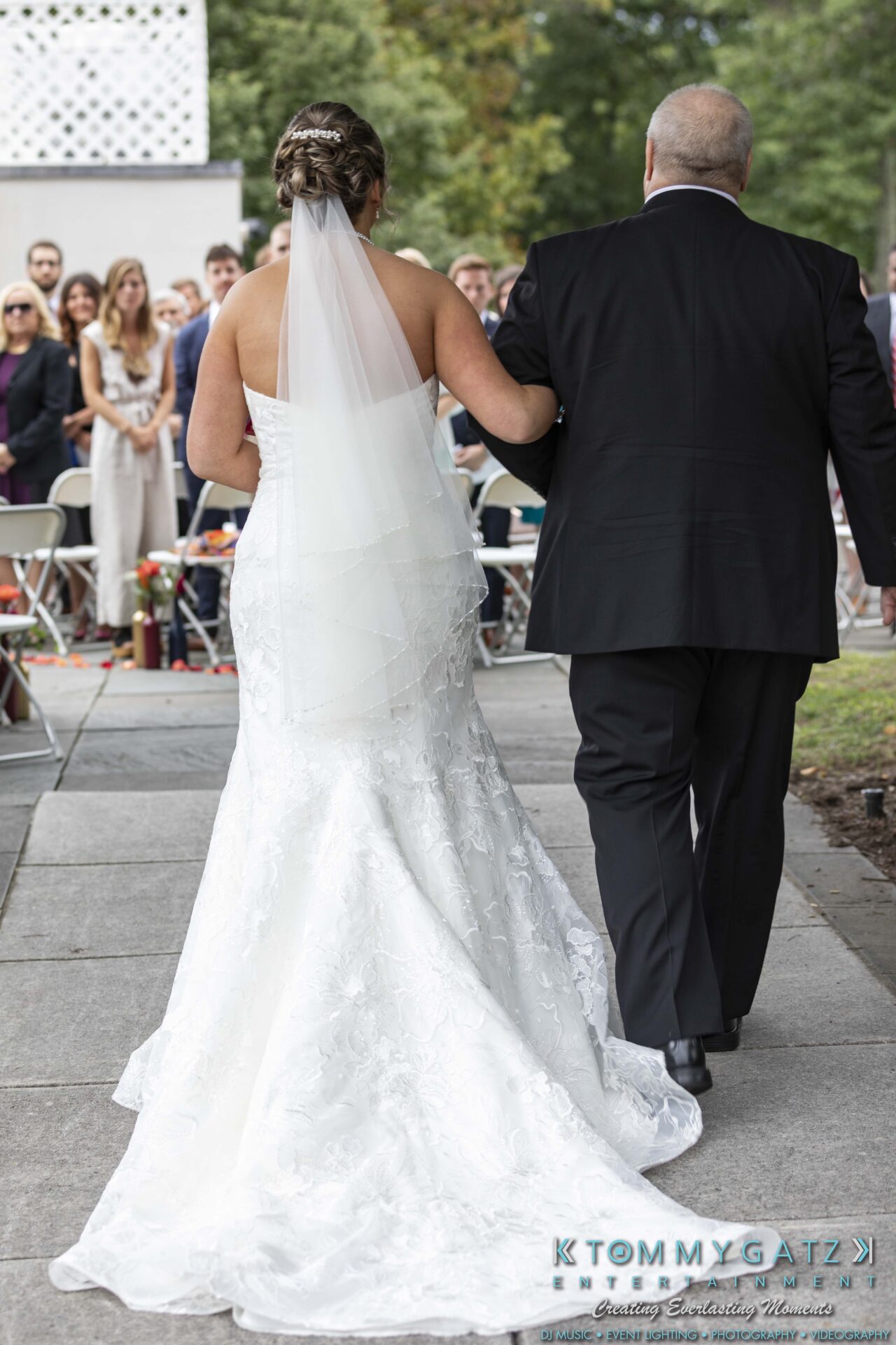 Lisa-Robert-092218-BLOG-selections-WM-48 - TOMMY GATZ ENTERTAINMENT Bride in a white gown and veil walks down an outdoor aisle with an older man, while guests watch in the background.