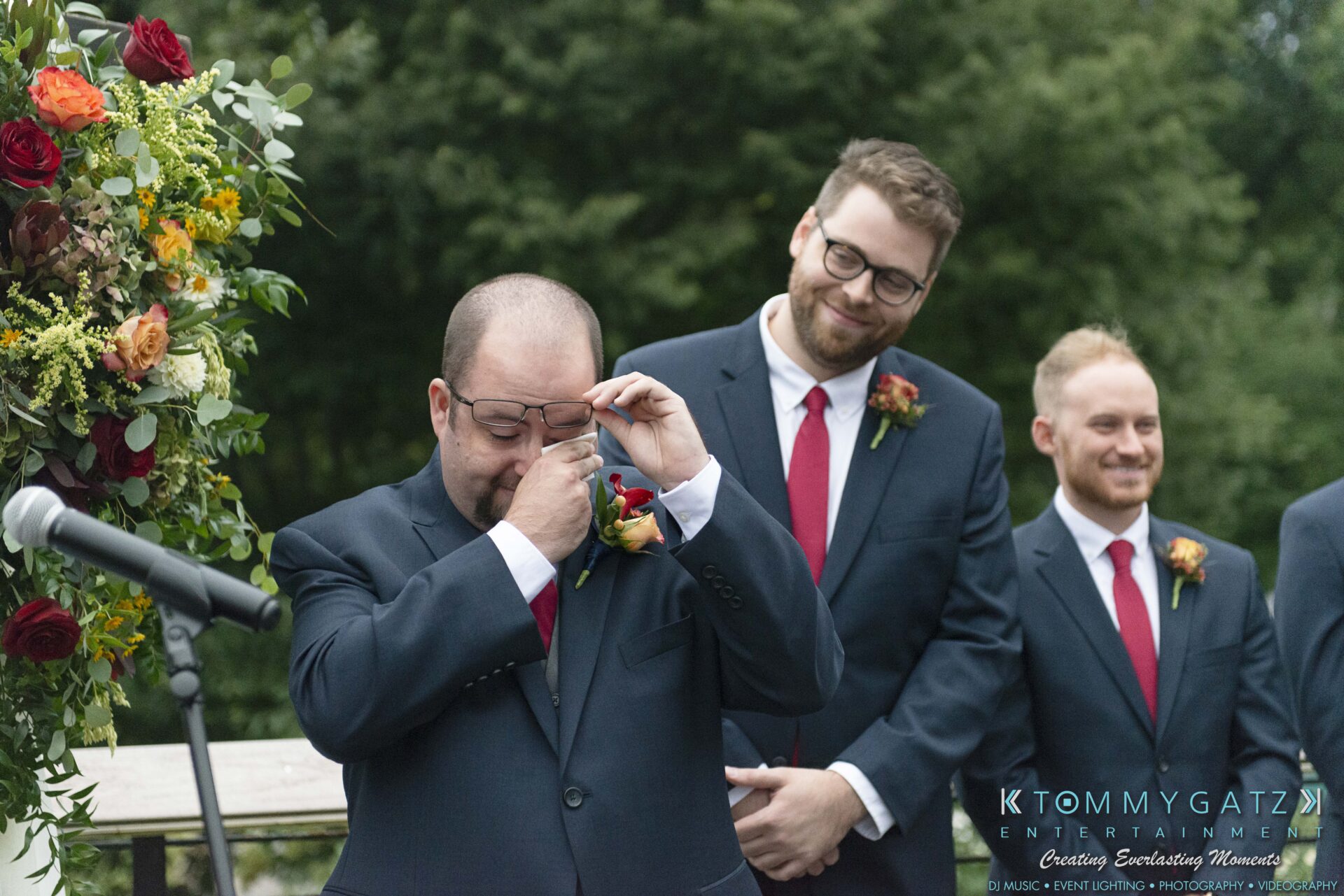 Lisa-Robert-092218-BLOG-selections-WM-51 - TOMMY GATZ ENTERTAINMENT A man in a suit wipes his tears, standing beside two men in suits and red ties. A flower arrangement and microphone are seen in the background.