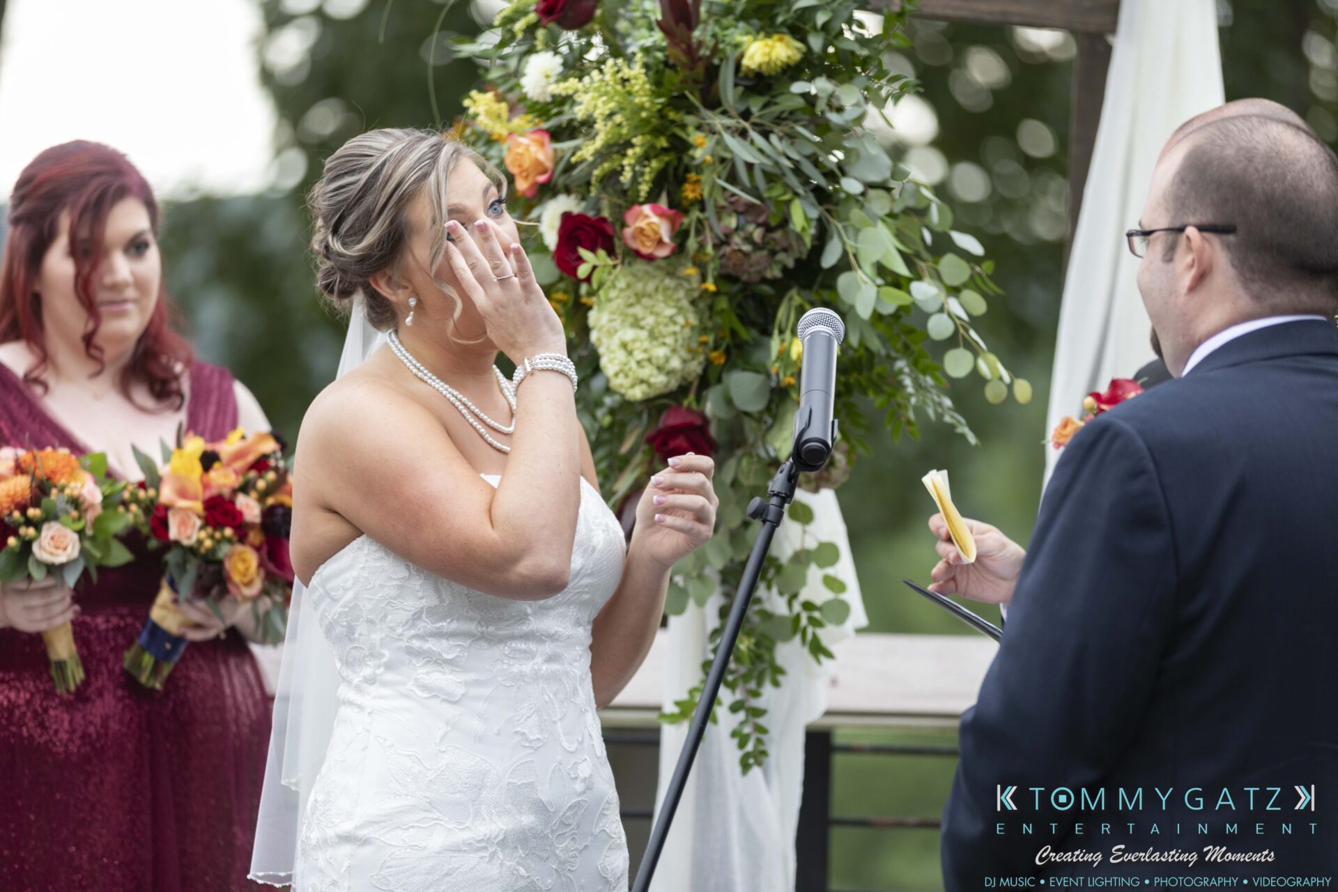 Lisa-Robert-092218-BLOG-selections-WM-55 - TOMMY GATZ ENTERTAINMENT A bride wipes a tear during an outdoor wedding ceremony. A groom reads from notes. A bridesmaid holds a bouquet nearby.