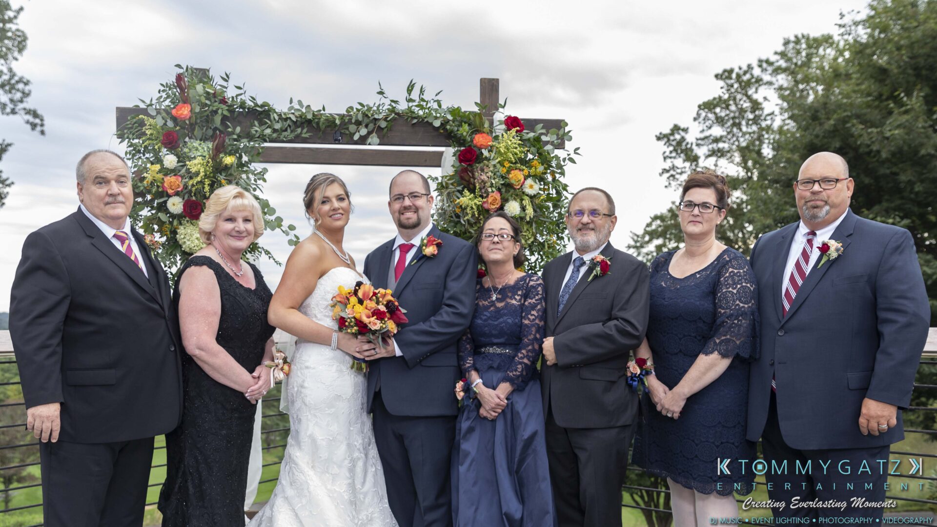 Lisa-Robert-092218-BLOG-selections-WM-63 - TOMMY GATZ ENTERTAINMENT A wedding group photo with the bride, groom, and six relatives standing in front of a floral arch outdoors.