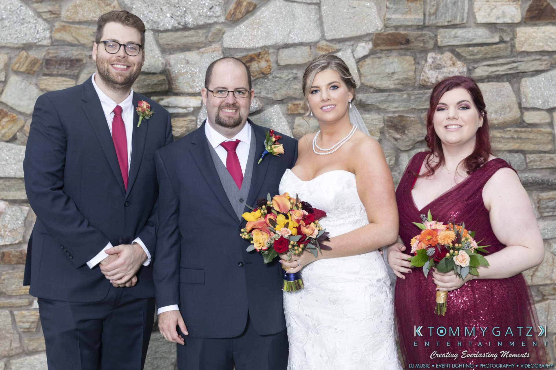Lisa-Robert-092218-BLOG-selections-WM-72 - TOMMY GATZ ENTERTAINMENT Four people pose in formal attire at an event, with two holding flower bouquets. A stone wall serves as the backdrop.