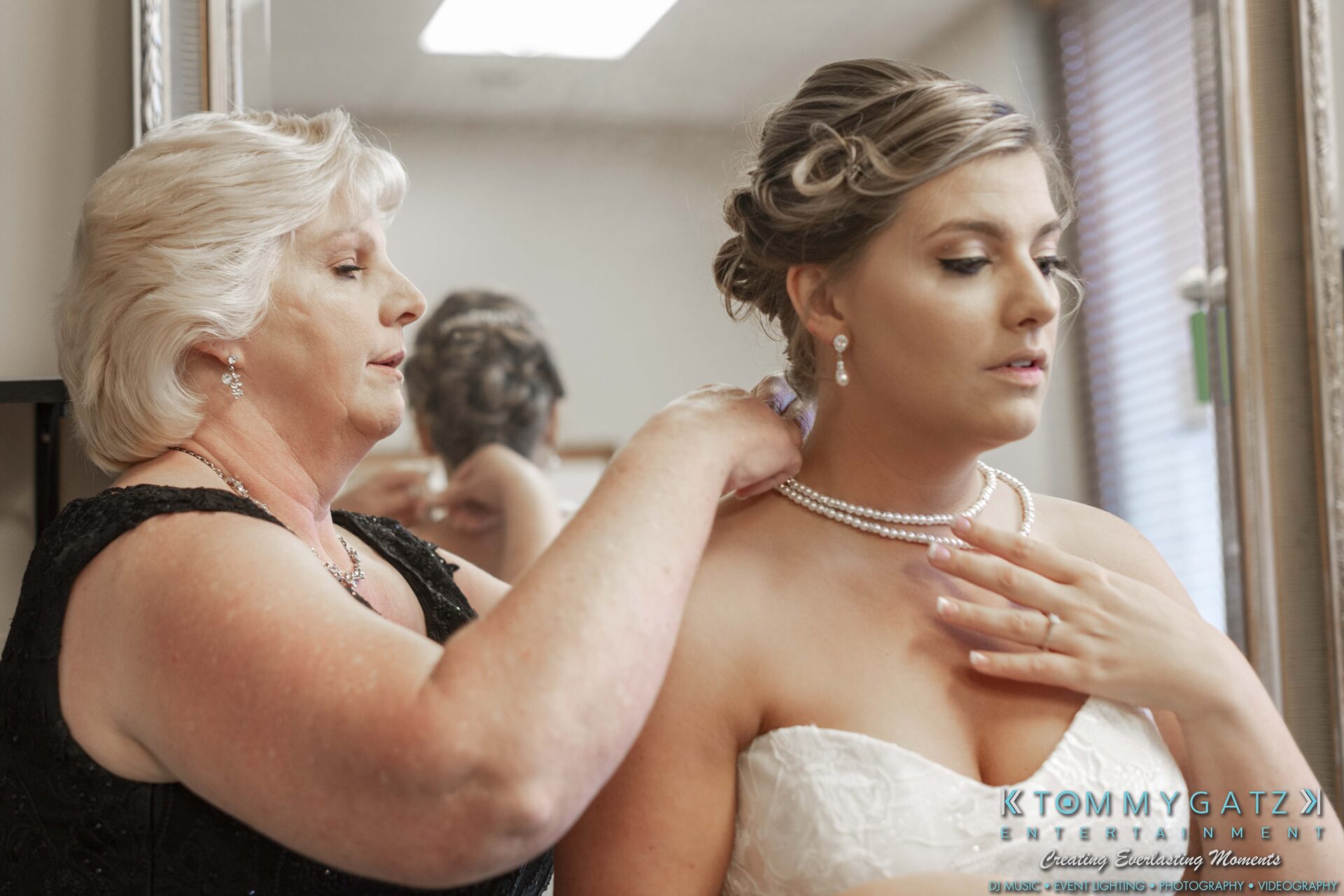 Lisa-Robert-092218-BLOG-selections-WM-8 - TOMMY GATZ ENTERTAINMENT A woman helps another woman in a white dress adjust her necklace in front of a mirror.