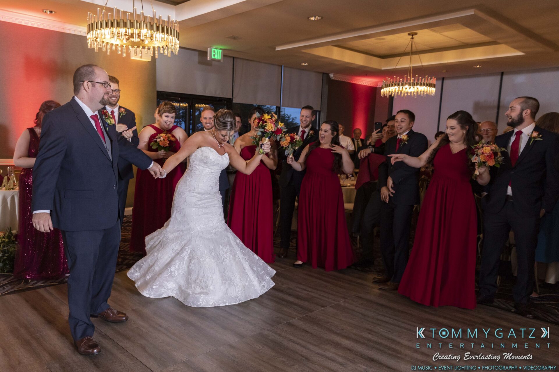 Lisa-Robert-092218-BLOG-selections-WM-85 - TOMMY GATZ ENTERTAINMENT A bride in a white gown dances with a groom in a suit, surrounded by a group of people in red dresses and suits, inside a decorated event venue.