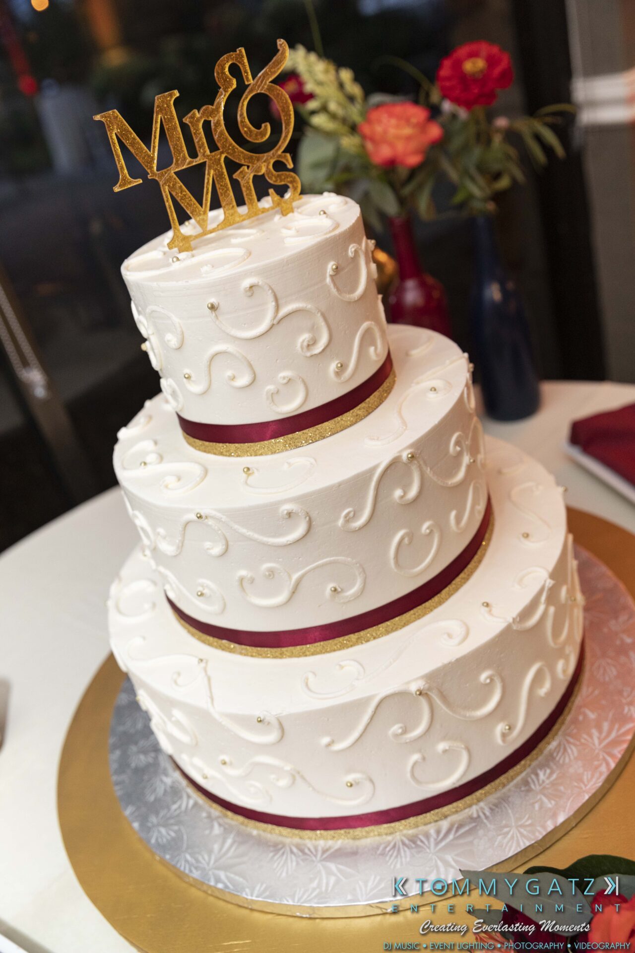 Lisa-Robert-092218-BLOG-selections-WM-87 - TOMMY GATZ ENTERTAINMENT Three-tier white wedding cake with red ribbon accents and a "Mr & Mrs" topper, on a silver and gold base.