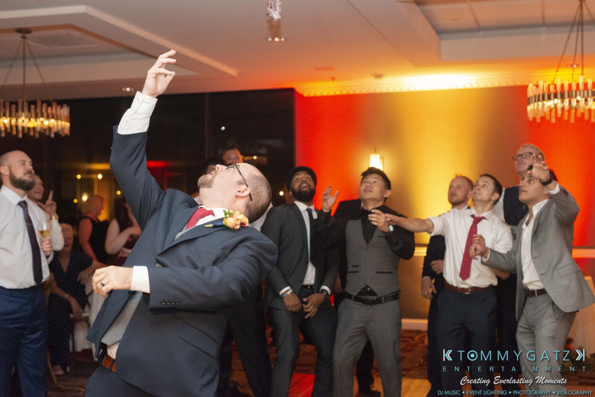 Lisa-Robert-092218-BLOG-selections-WM-99 - TOMMY GATZ ENTERTAINMENT A group of people in formal attire are enthusiastically reaching upwards at an indoor event with colorful lighting.