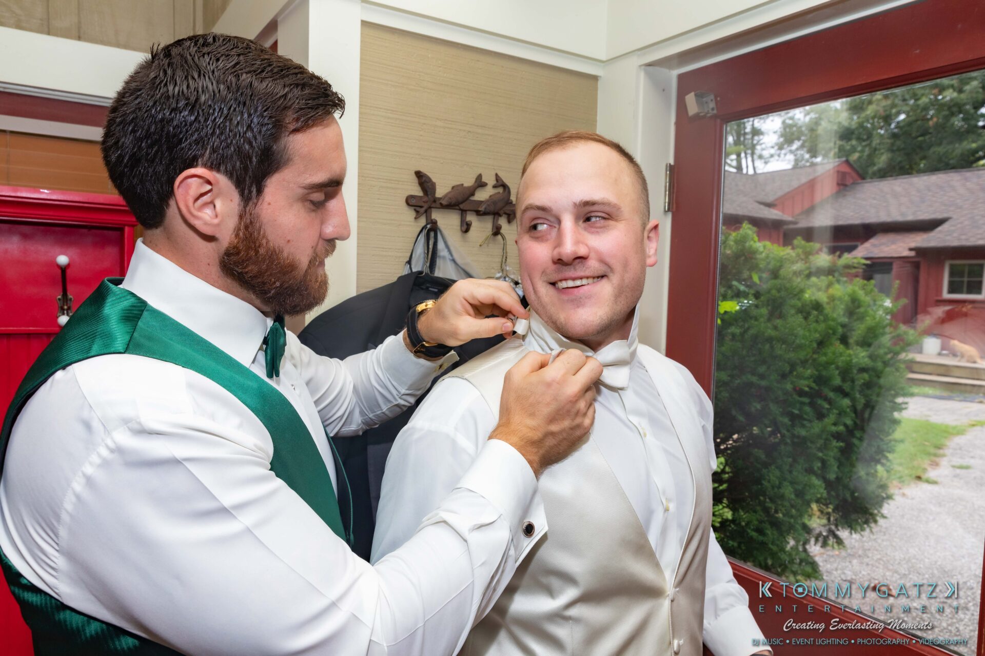 Proctor-Wedding-HIGHLIGHTS-091419-19 - TOMMY GATZ ENTERTAINMENT A man in a green vest helps another man adjust his bow tie in a room.
