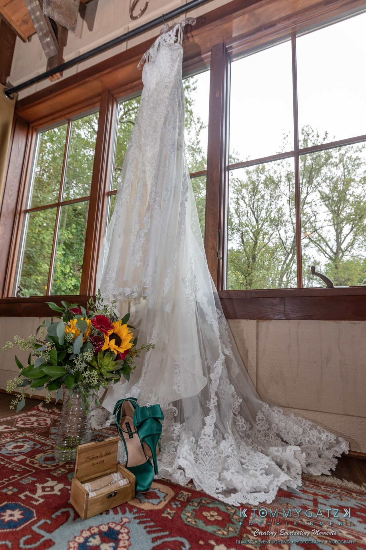 Proctor-Wedding-HIGHLIGHTS-091419-6 - TOMMY GATZ ENTERTAINMENT A lace wedding dress hangs near a large window. Beside it are a bouquet of flowers, teal high heels, and a small wooden box.