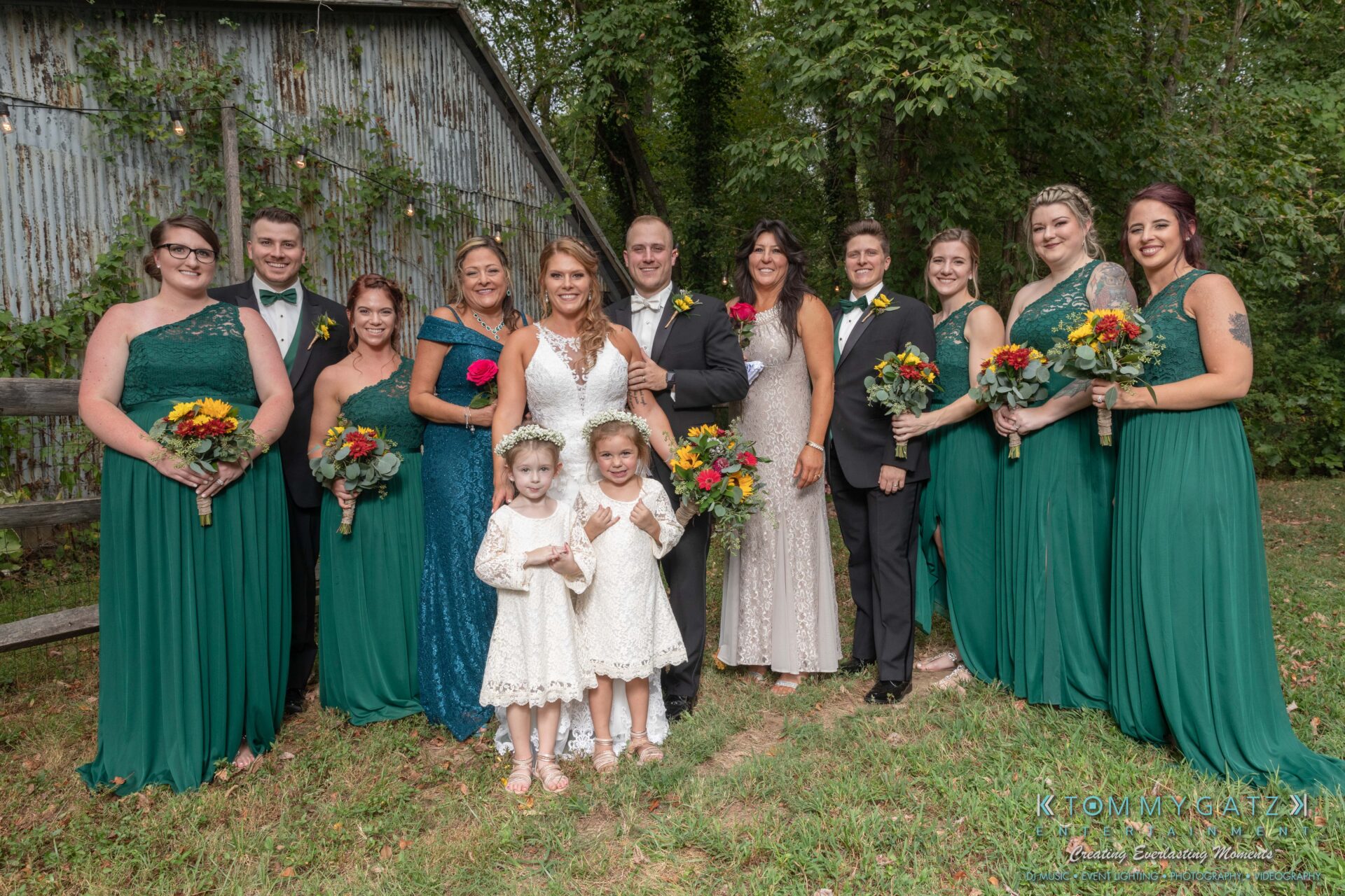 Proctor-Wedding-HIGHLIGHTS-091419-63 - TOMMY GATZ ENTERTAINMENT A wedding party poses outdoors; the group includes bridesmaids in green dresses, groomsmen in suits, two flower girls in white dresses, and a bride and groom.