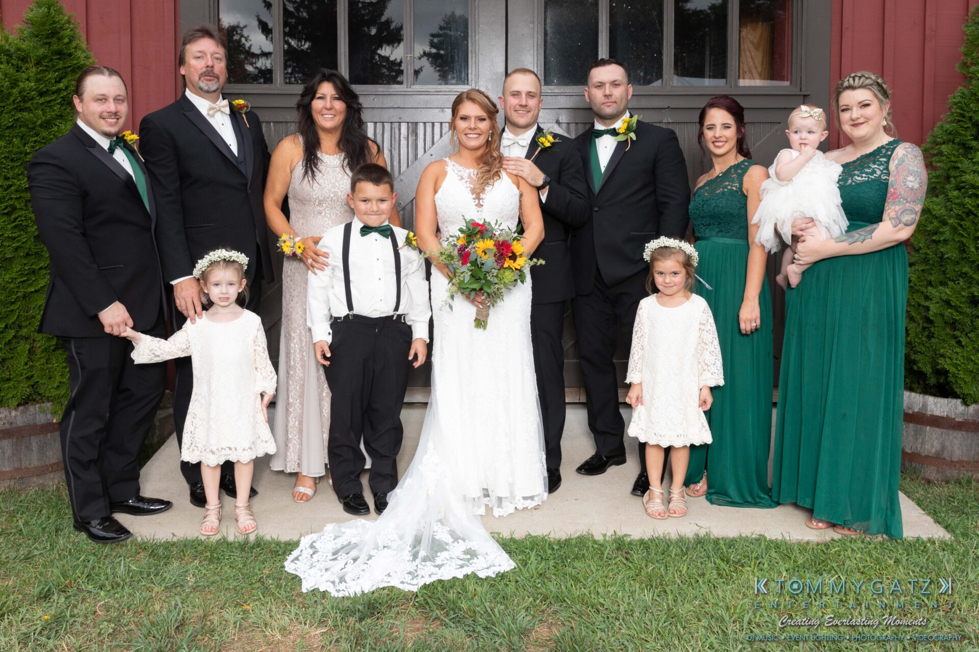 Proctor-Wedding-HIGHLIGHTS-091419-72 - TOMMY GATZ ENTERTAINMENT A wedding party poses for a group photo outdoors. The bride and groom stand center, surrounded by flower girls, a ring bearer, bridesmaids, and groomsmen.