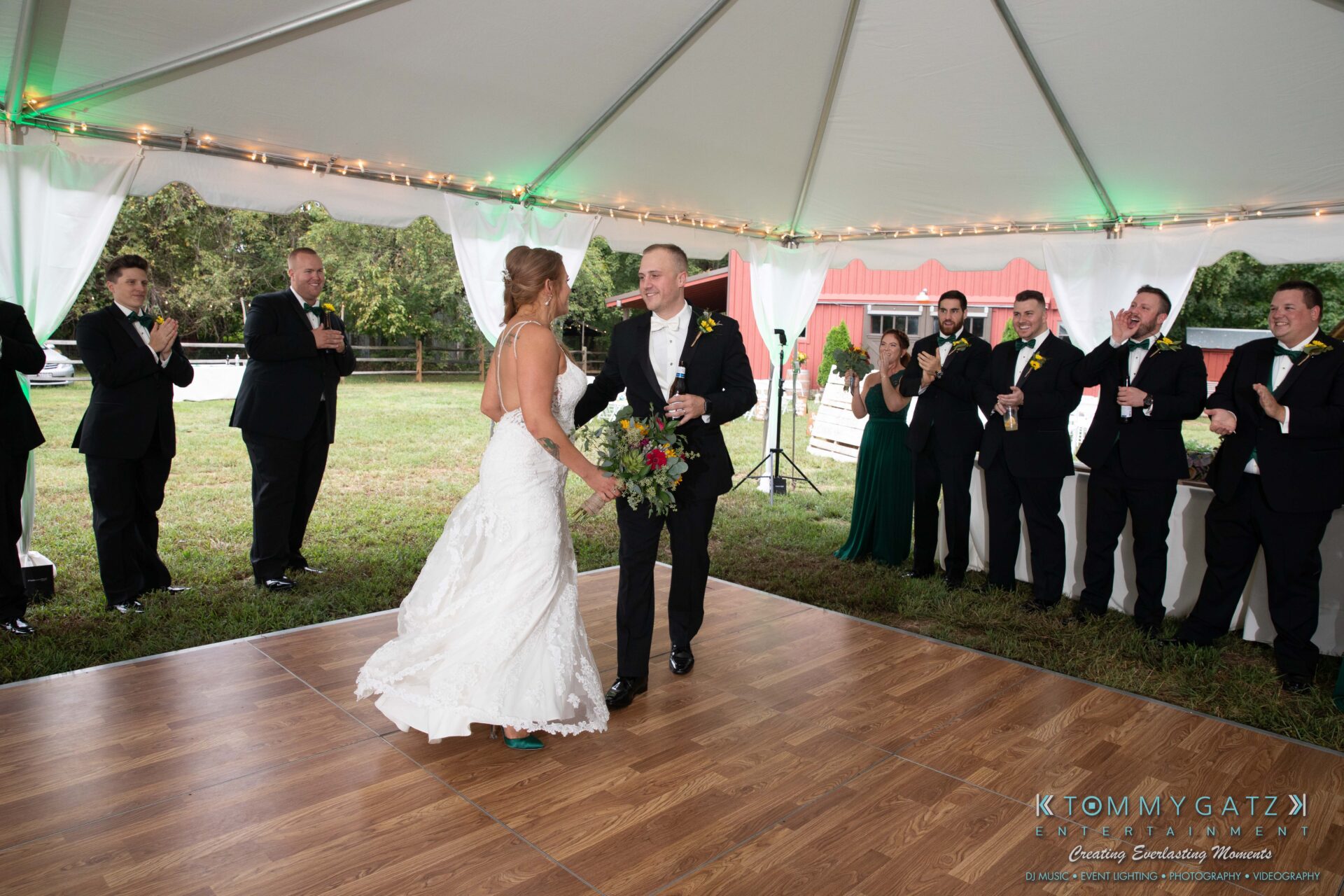 Proctor-Wedding-HIGHLIGHTS-091419-82 - TOMMY GATZ ENTERTAINMENT A bride and groom dance under a tent while guests in formal attire stand around and clap.
