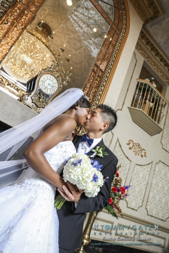 A bride and groom kiss indoors, standing near a vintage clock, with the bride holding a bouquet.