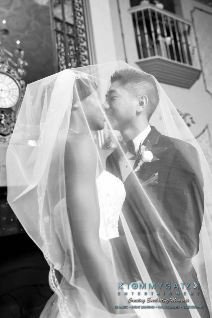 Bride and groom sharing a kiss under a veil in a black-and-white photograph, with decorative background and visible clock.
